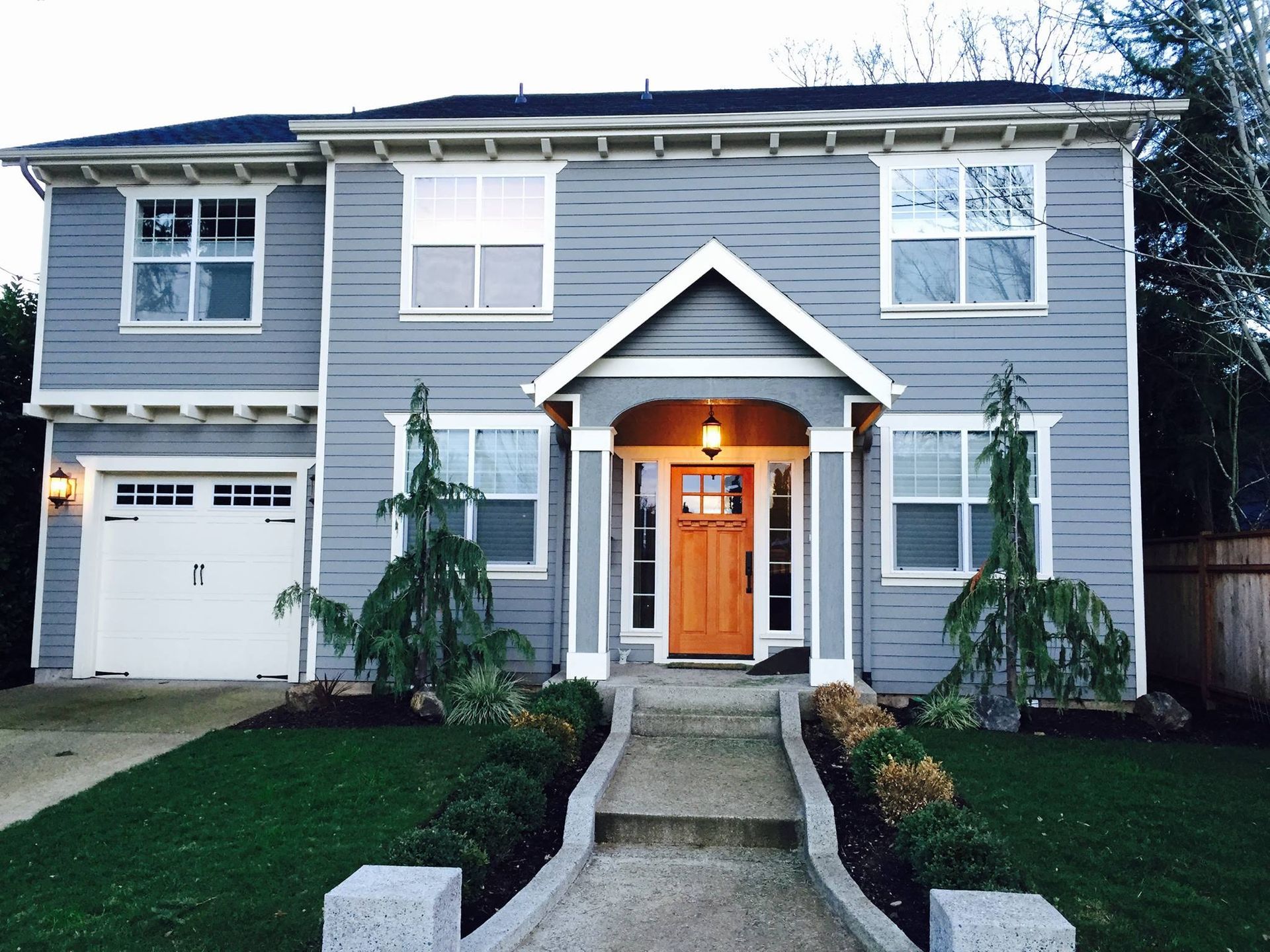 Two-story blue house with white trim, wooden door, and green lawn.