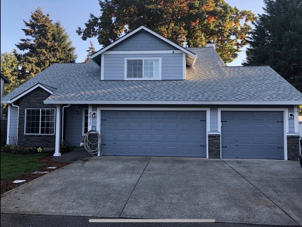 Blue house with gray roof and three-car garage, stone accents, concrete driveway, front yard.
