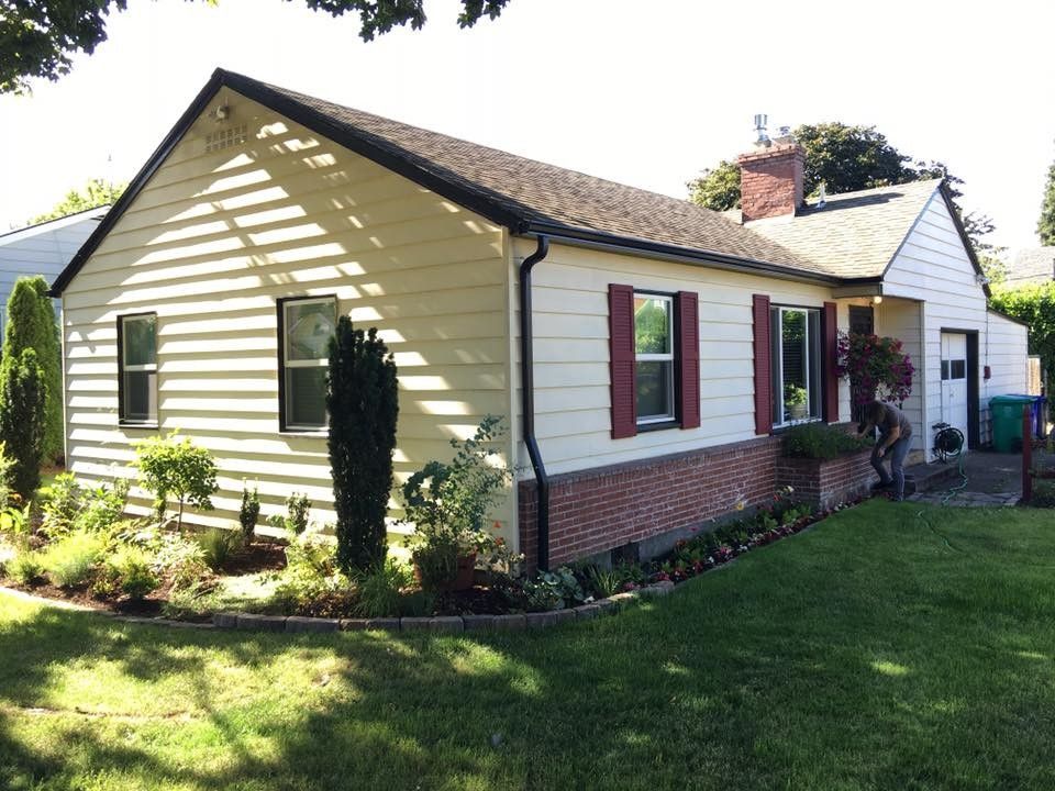 Yellow house with brick base, red shutters, and green lawn.