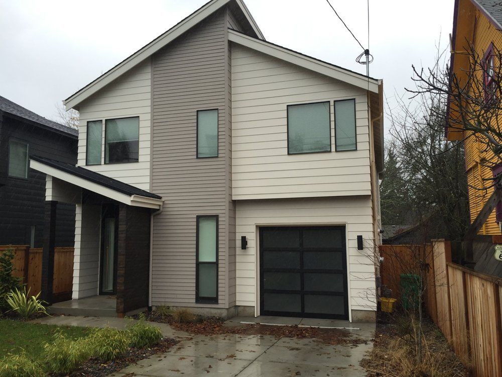 Two-story modern home with gray and beige siding, black garage door, and small lawn.