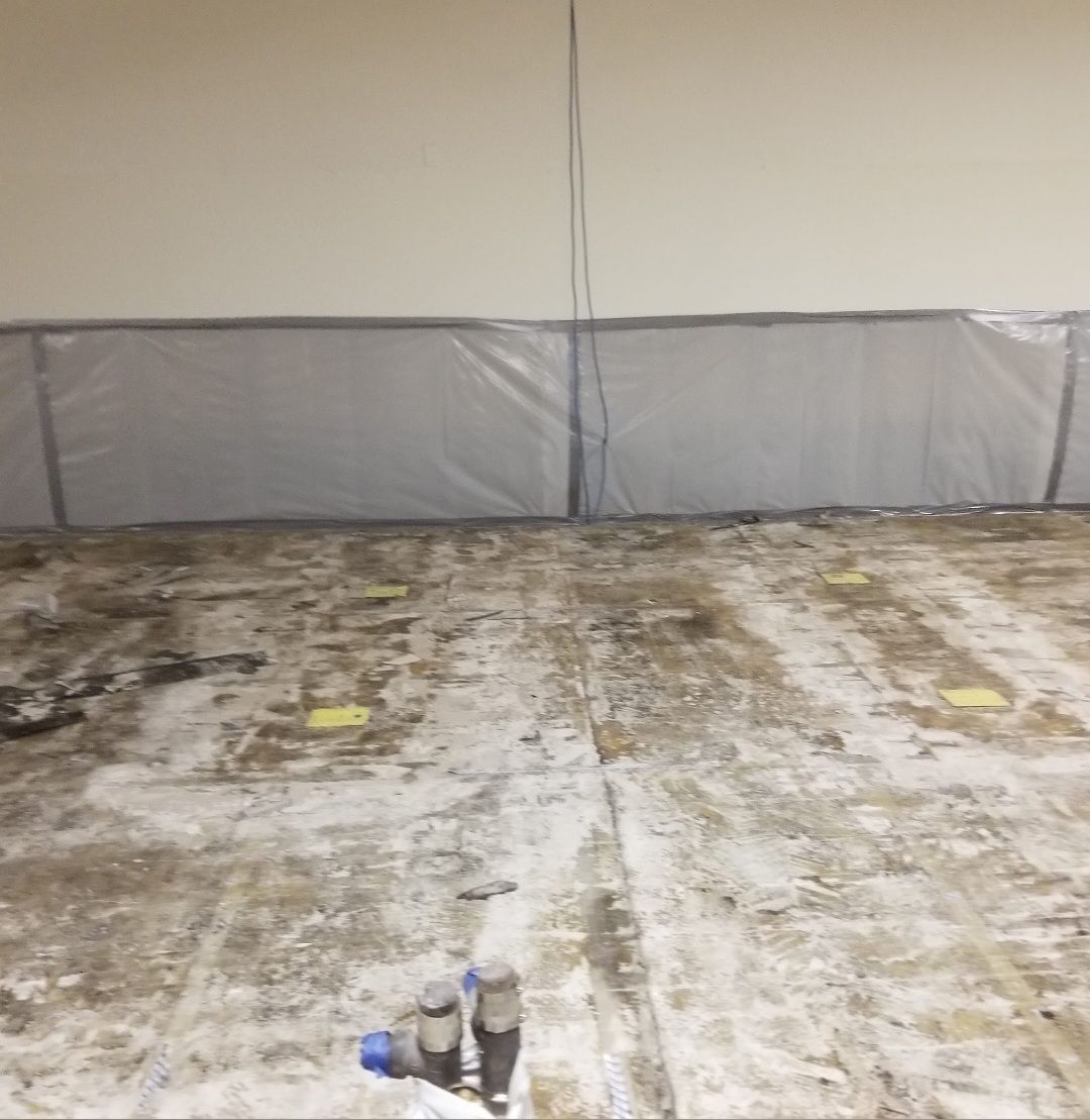 Dirty wooden floor with water stains, plastic barrier on wall, and pipes in a bare room.