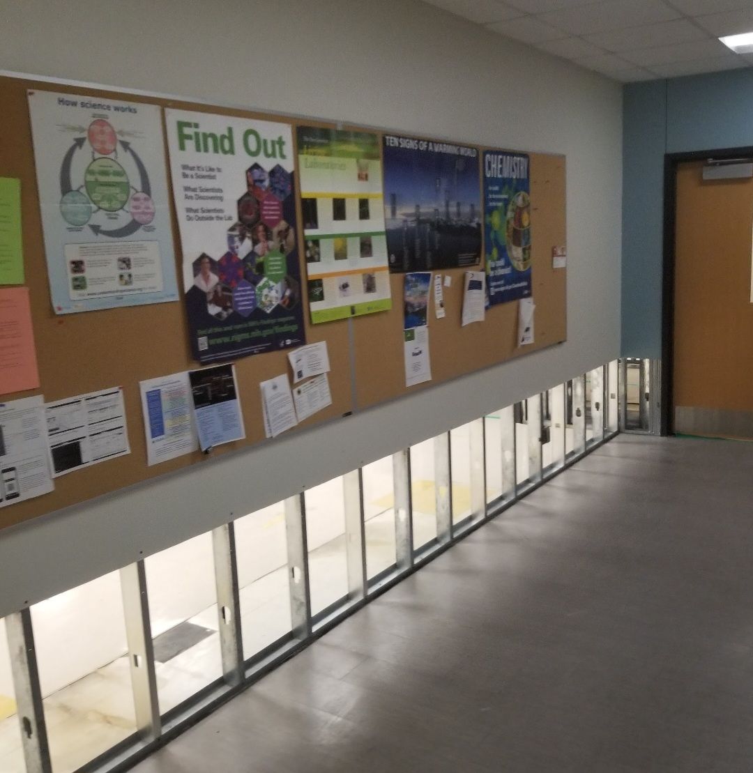 Hallway with bulletin board, clear glass barrier, and door.