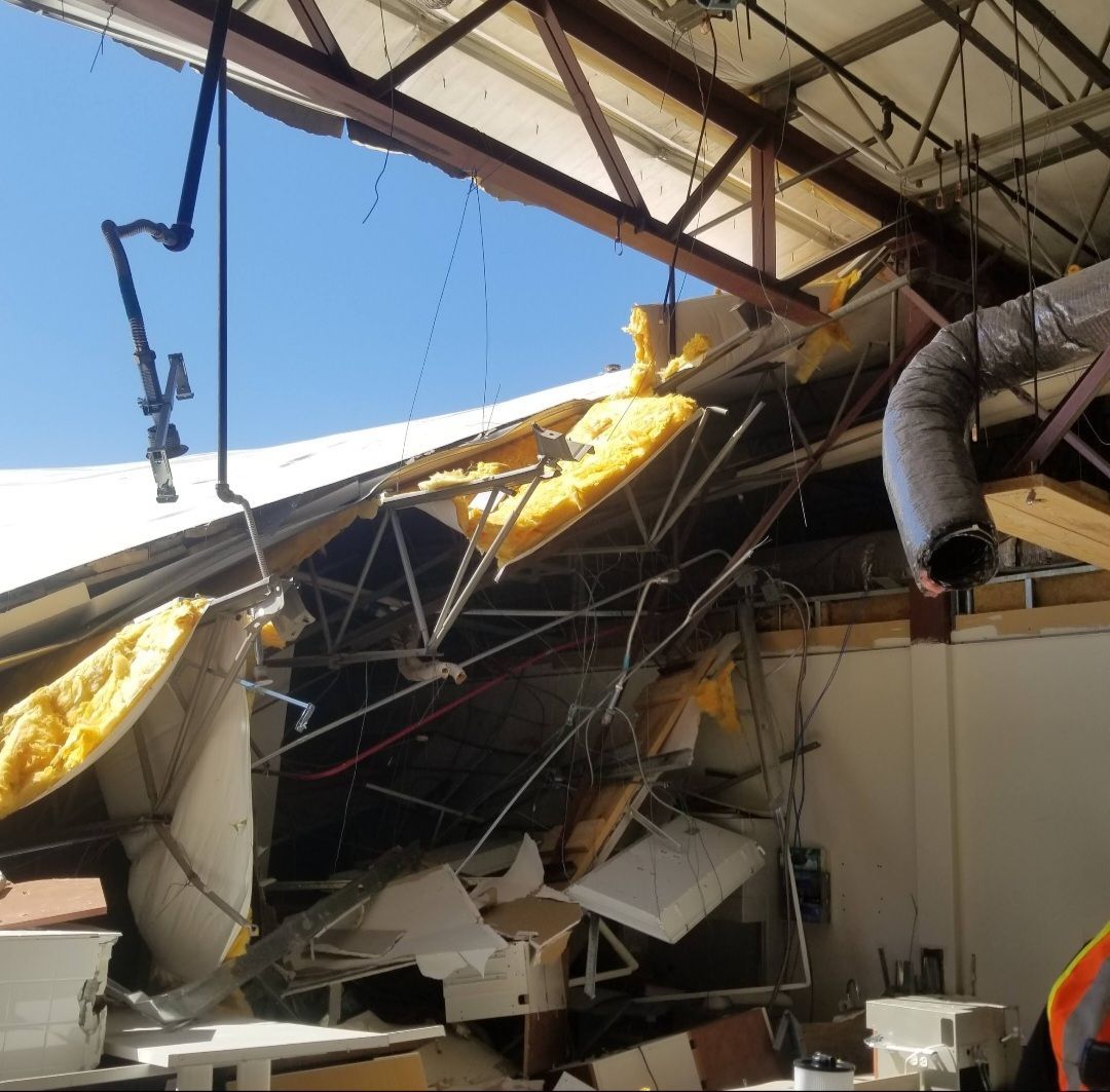 Damaged industrial building; roof collapsed, exposing insulation and structural beams against blue sky.