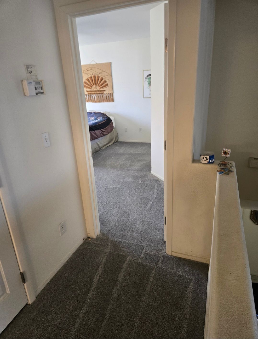 Hallway leading to bedroom with bed and art, gray carpet.