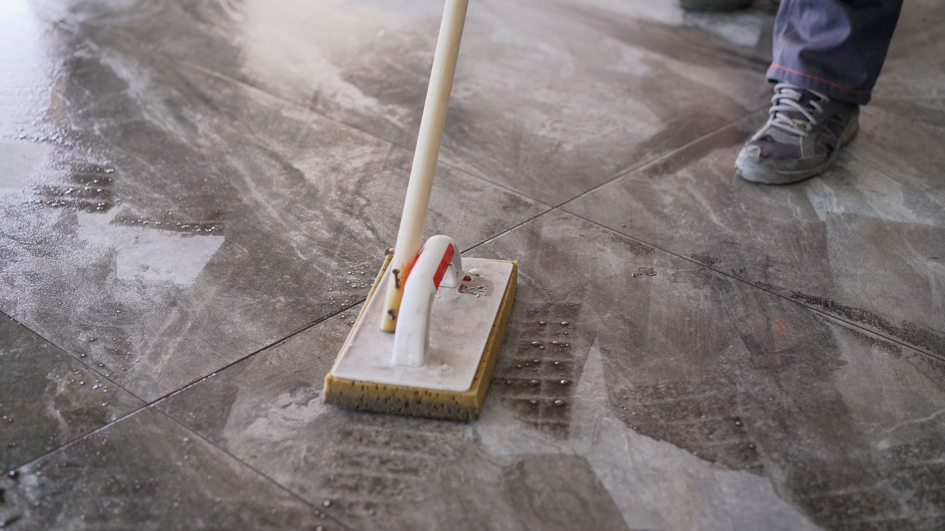 Person using a grout brush to clean gray tiled floor.