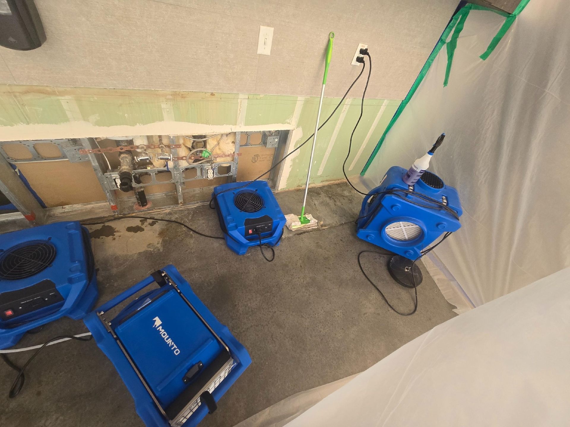 Dehumidifiers and equipment drying a flooded interior space. Blue and gray tones, wires, wall damage.