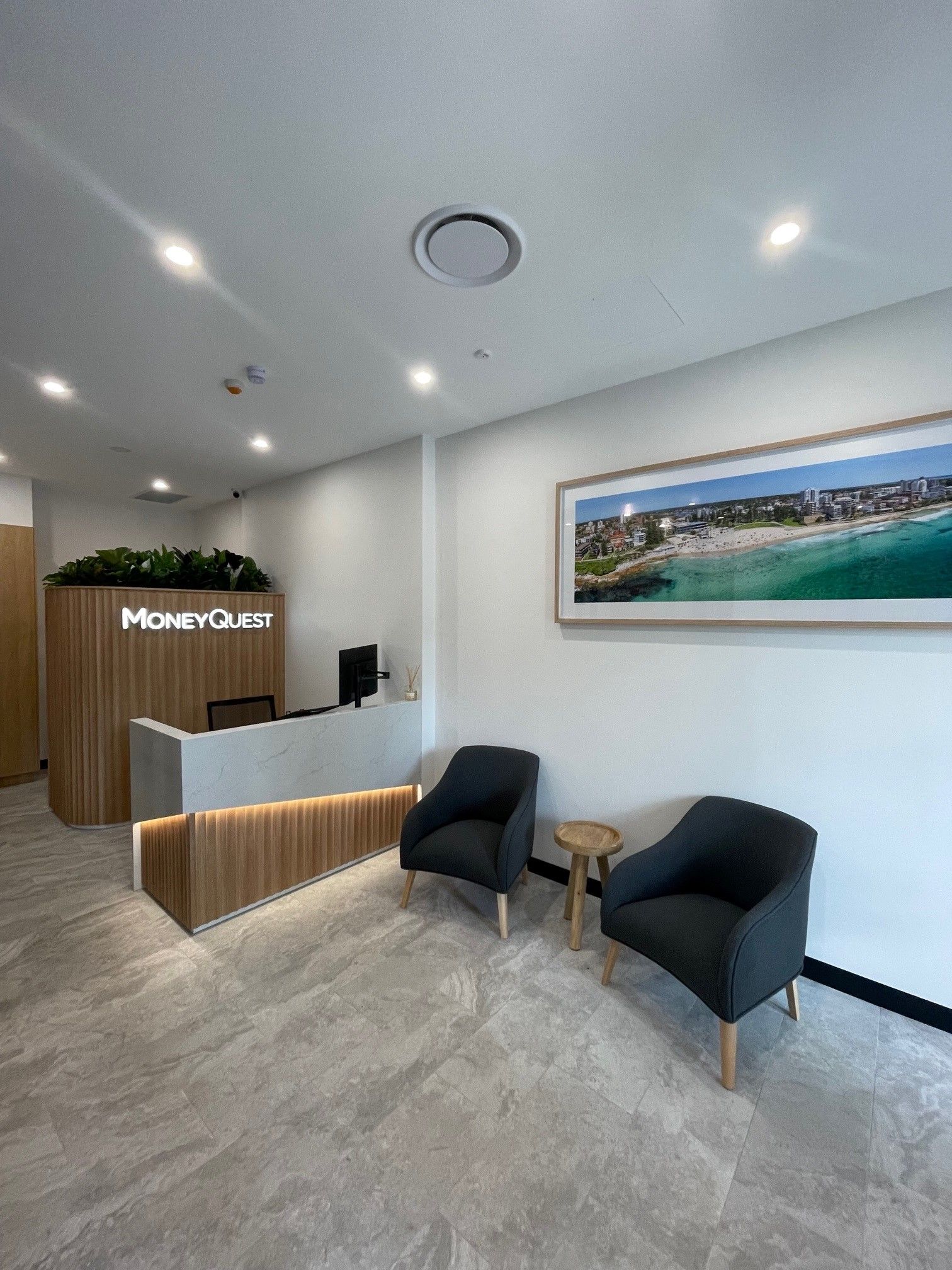 Modern office reception area with two armchairs, a small table, and a framed beach photo. The reception desk has a wooden front  — ATH Projects in Kirrawee, NSW