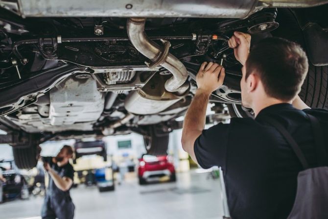 Mechanic inspecting a car’s undercarriage in a busy auto repair shop
