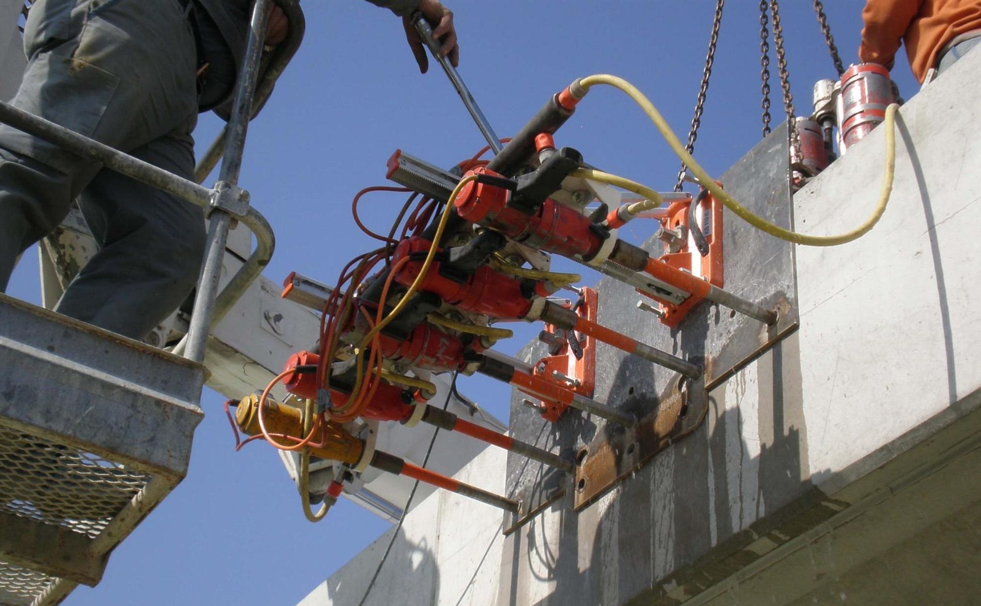 Von einer erhöhten Arbeitsplattform aus bedienen Bauarbeiter hydraulische Heber, um Bauteile aus Betonbrücken zu justieren.