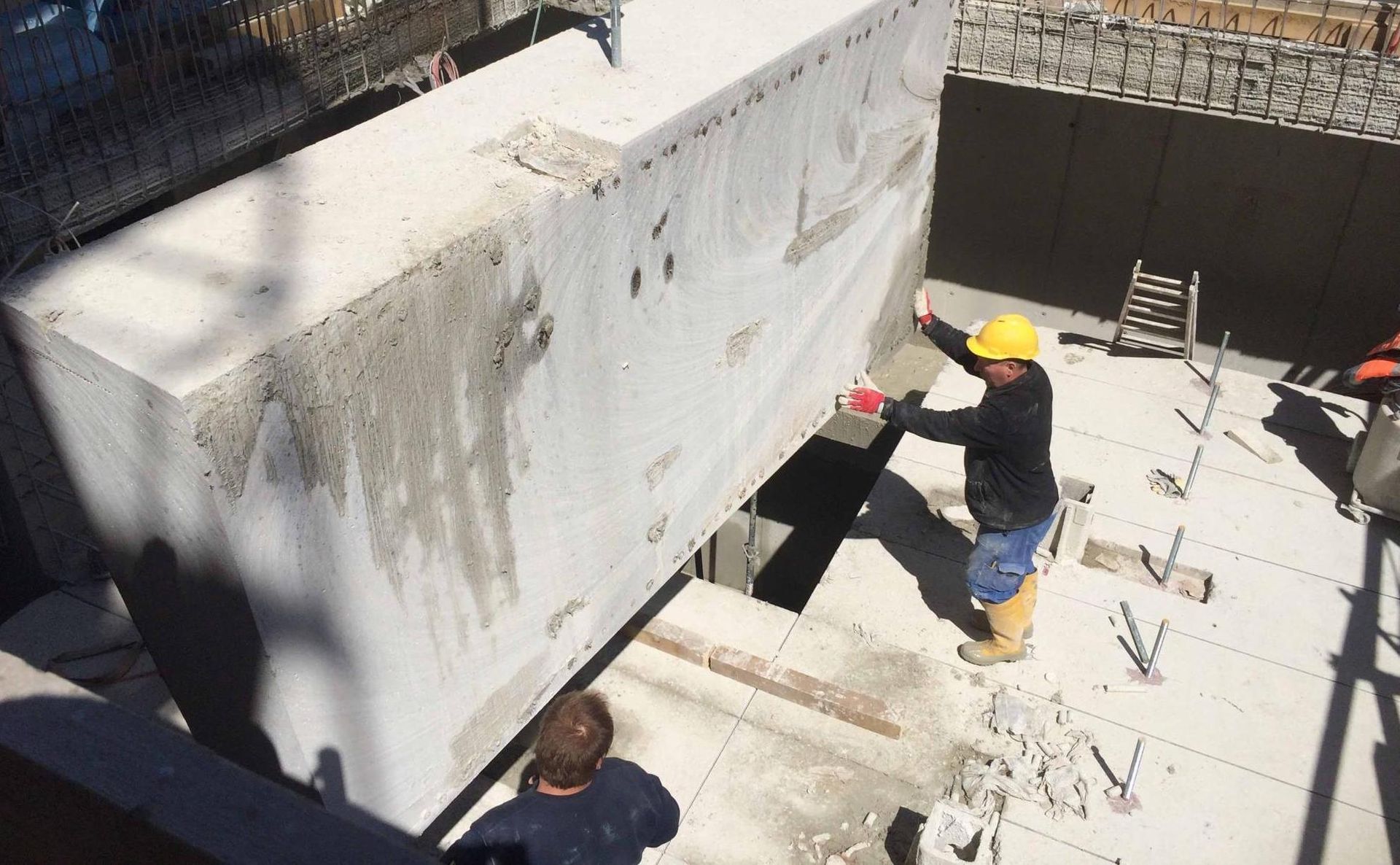 Zwei Bauarbeiter positionieren einen großen Betonblock auf einer aktiven Baustelle.