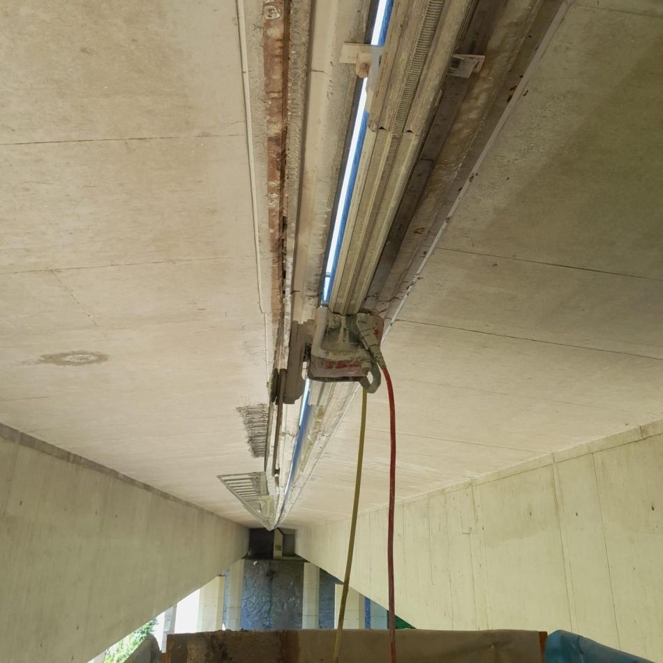 Unter einer Betonbrücke gleitet ein metallener Wagen auf einer befestigten Schiene entlang