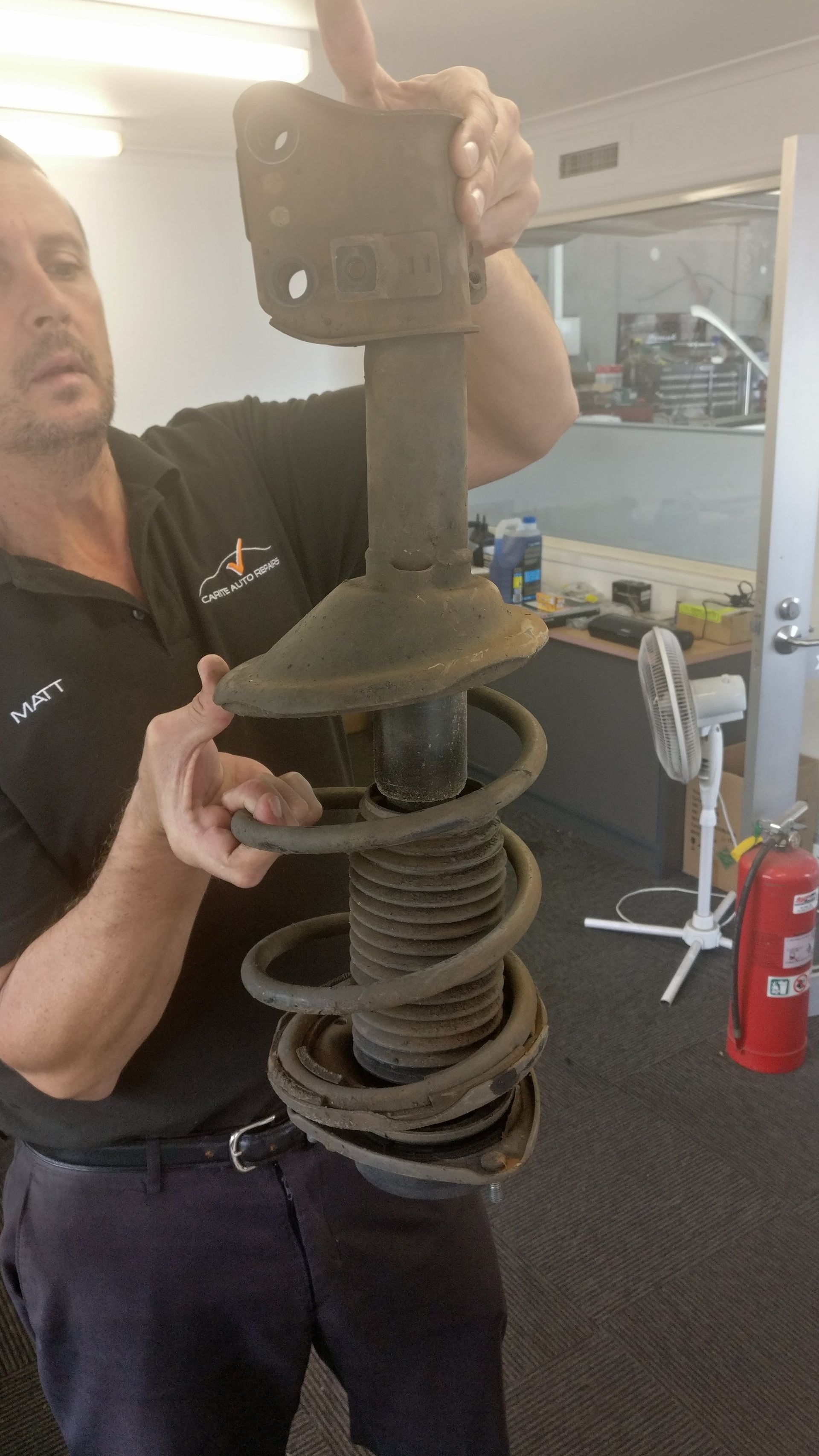 Mechanic Holding a Car Suspension Strut With Coil Spring — Carite Auto Repairs In Warana, QLD