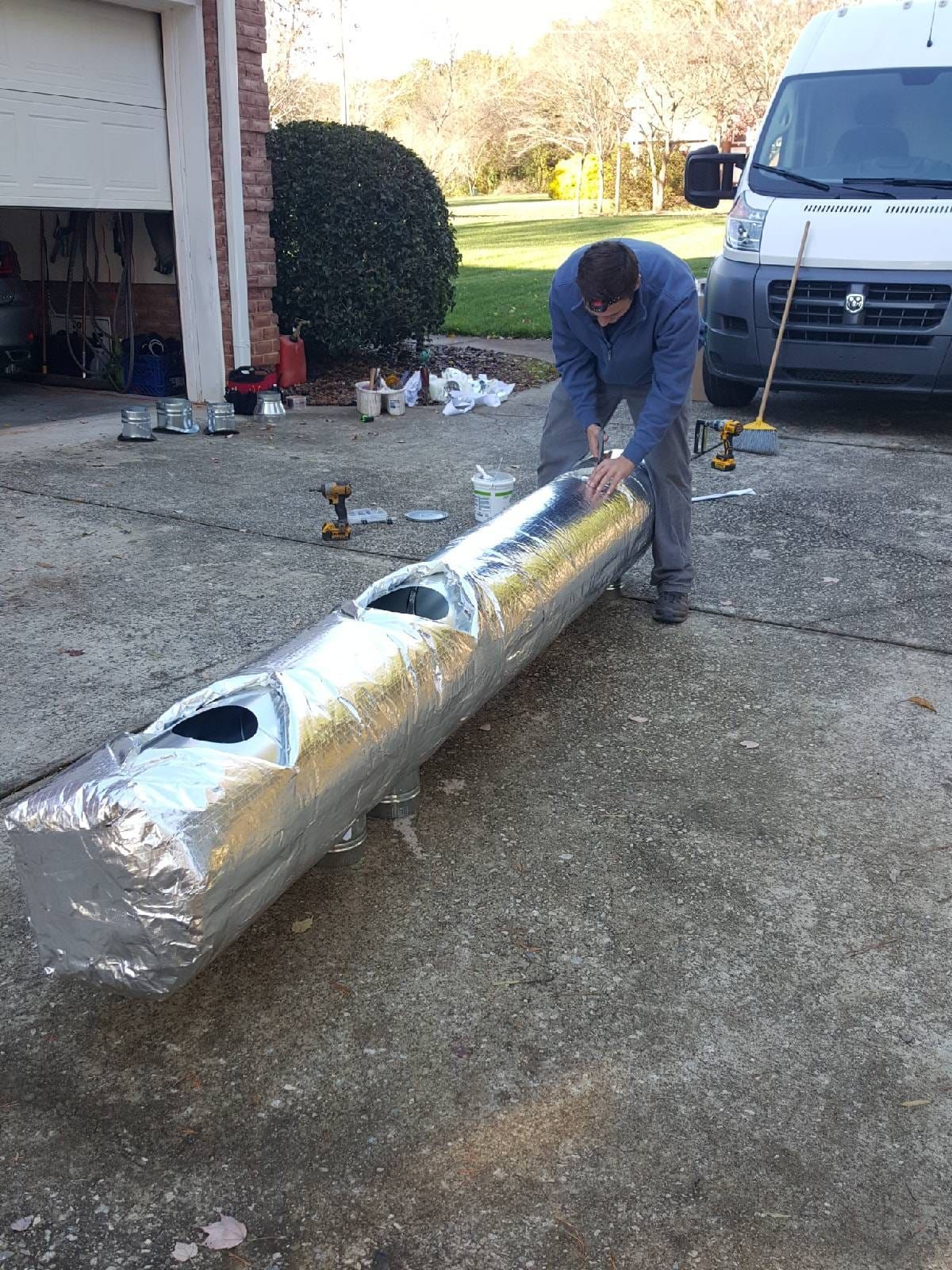 a man is standing next to a large pipe wrapped in aluminum foil .
