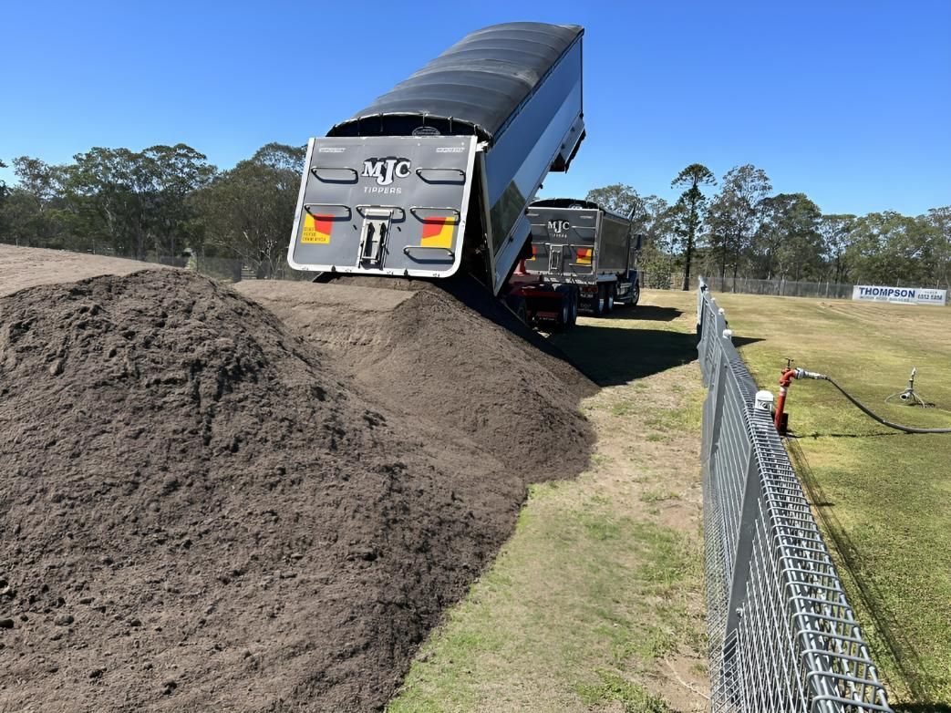 A Dump Truck is Driving Down a Dirt Road Next to a Fence — Manning Valley Landscapes in Forster, NSW