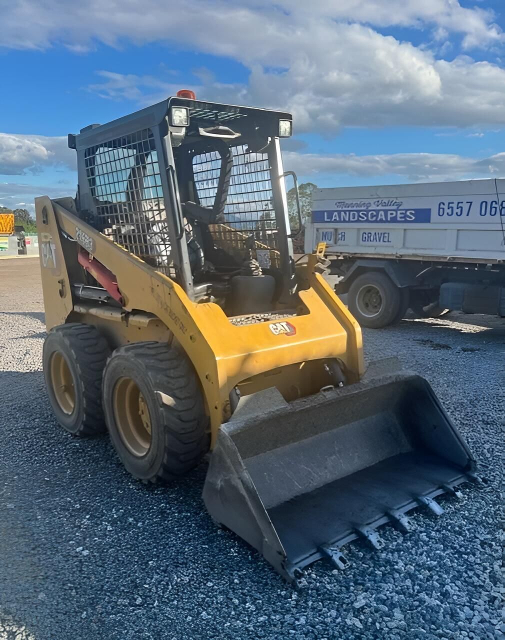 A Small Bulldozer is Parked on Gravel Next to a Truck — Manning Valley Landscapes in Wingham, NSW