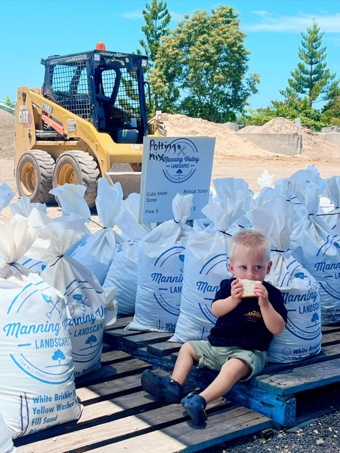 A Little Boy Is Sitting on A Wooden Pallet Next to Bags of Sand — Manning Valley Landscapes in Wingham, NSW 