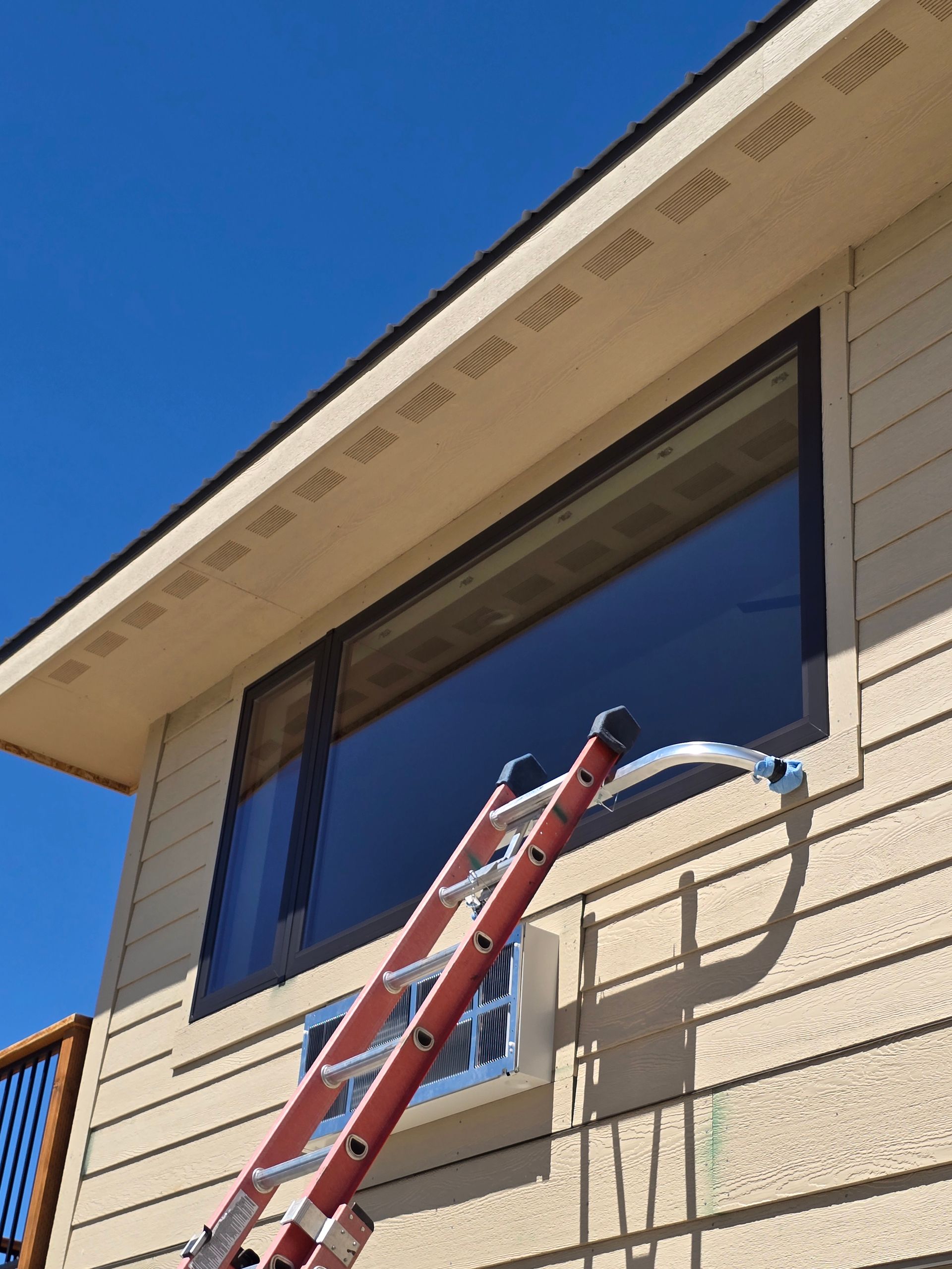 A red extension ladder leans against the exterior wall of a house, positioned just below a large rectangular window.
