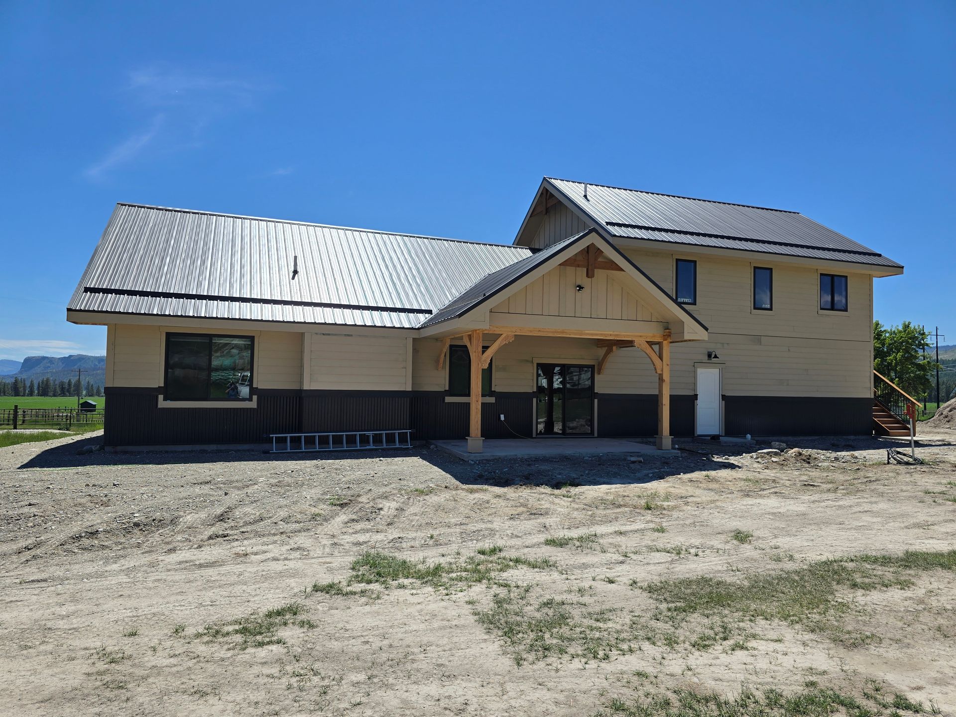 A newly constructed house with tan siding and a dark brown lower section under a metal roof, featuring a timber porch.