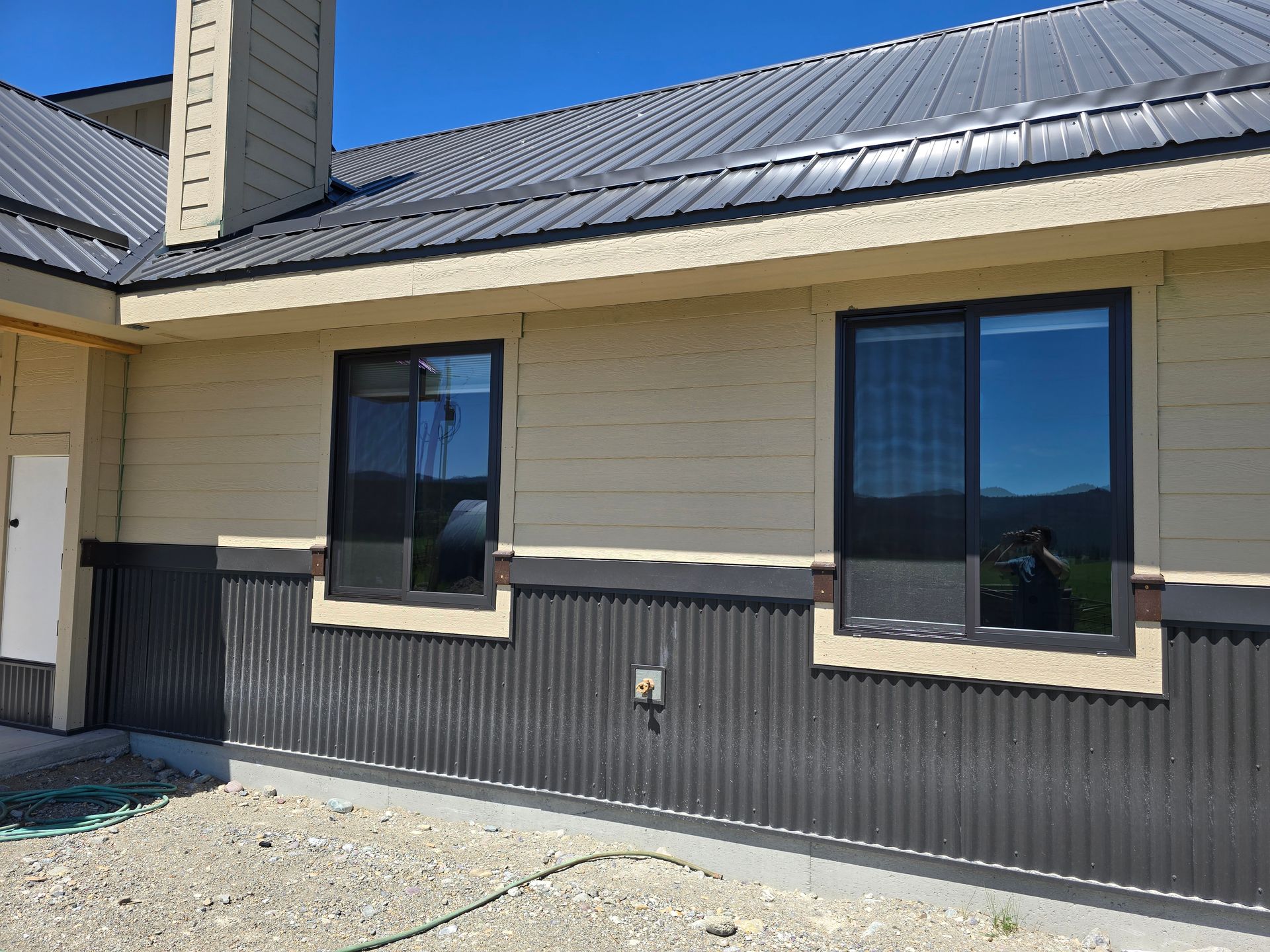 Exterior view of a house with tan siding over charcoal corrugated metal wainscoting and a matching metal roof.