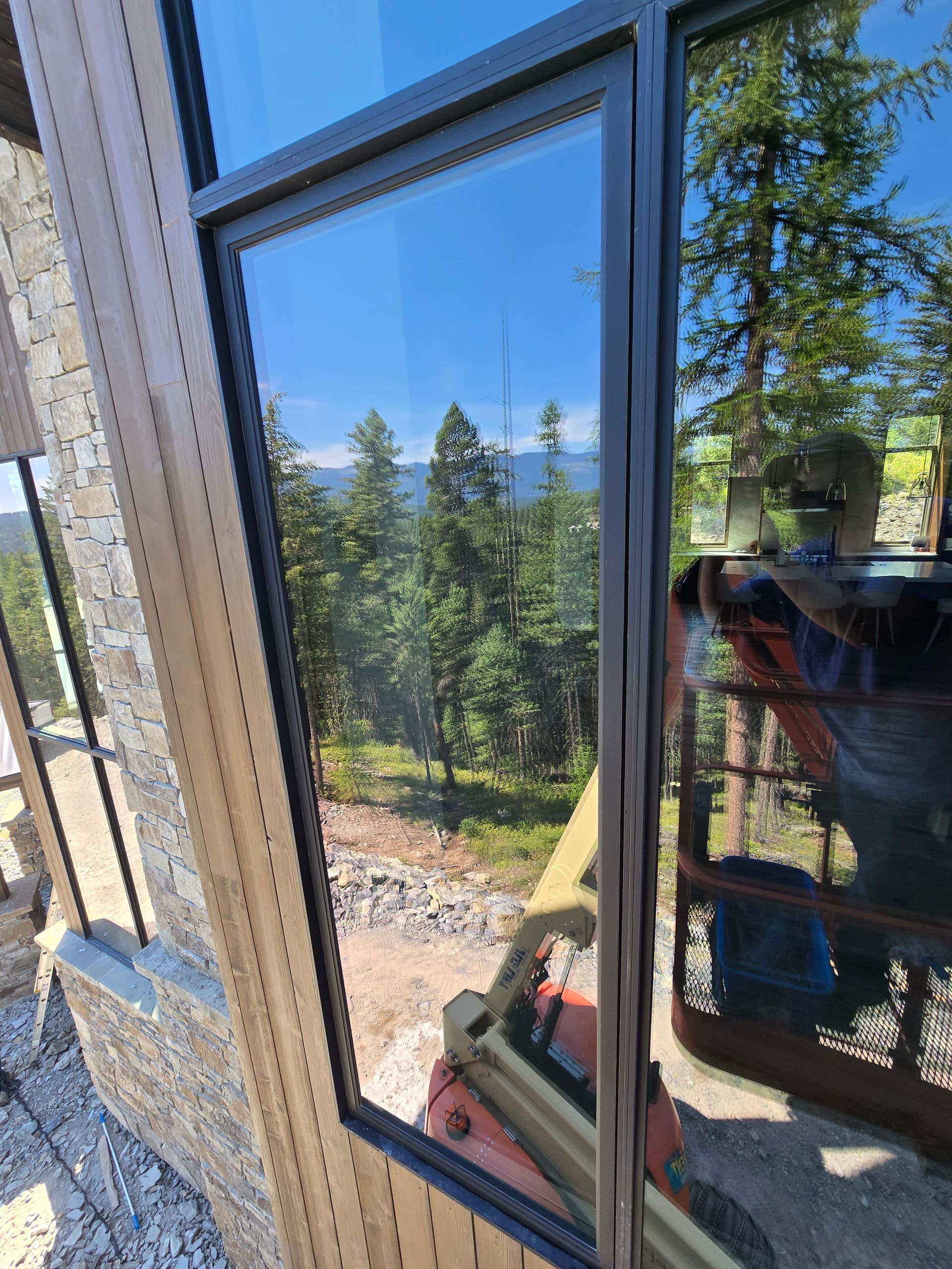 A view through a large window showing a sunny forest landscape and a construction lift parked outside.