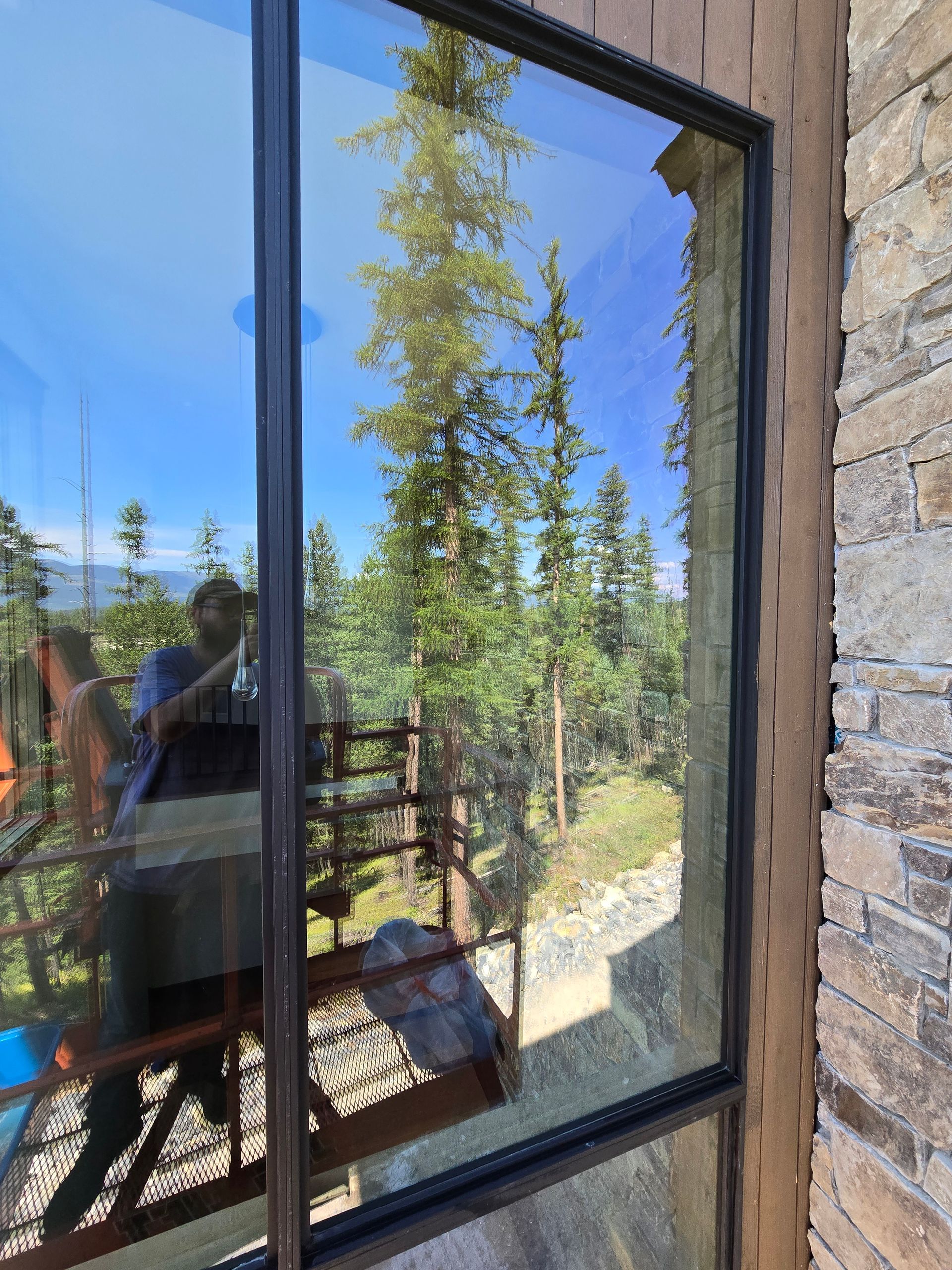 A window reflects a pine forest and a person working on construction scaffolding.