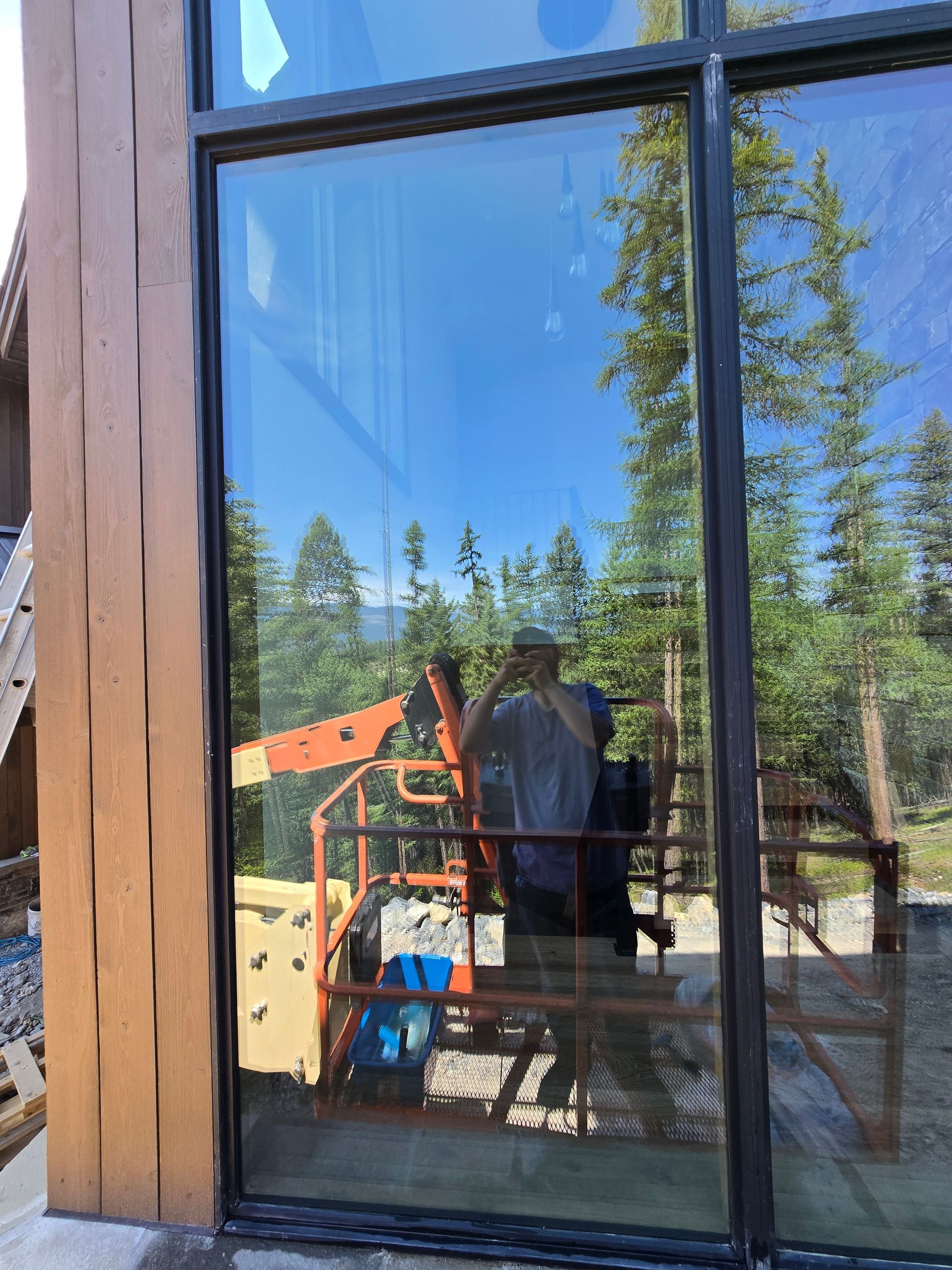 A person reflected in a large glass window of a building under construction, with a boom lift visible in the background.