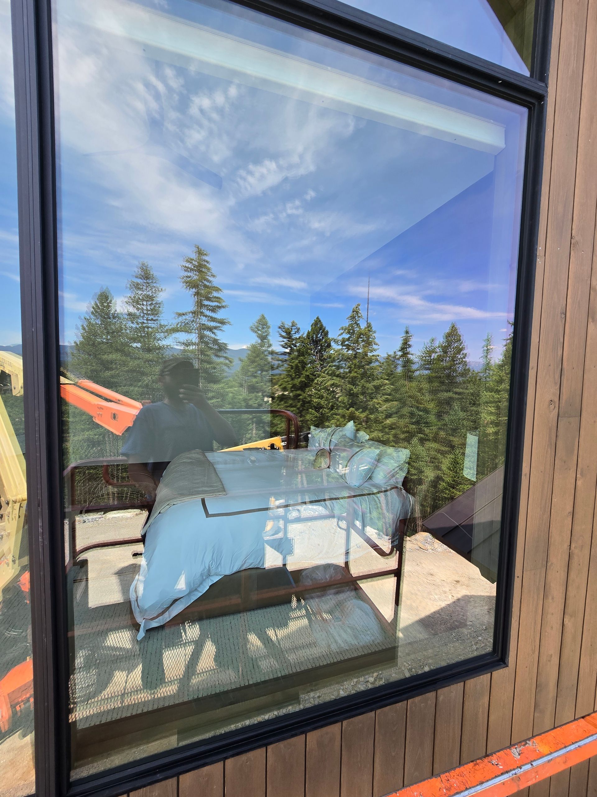 Reflection in a window showing an unmade bed inside a room with a view of trees and a blue sky.