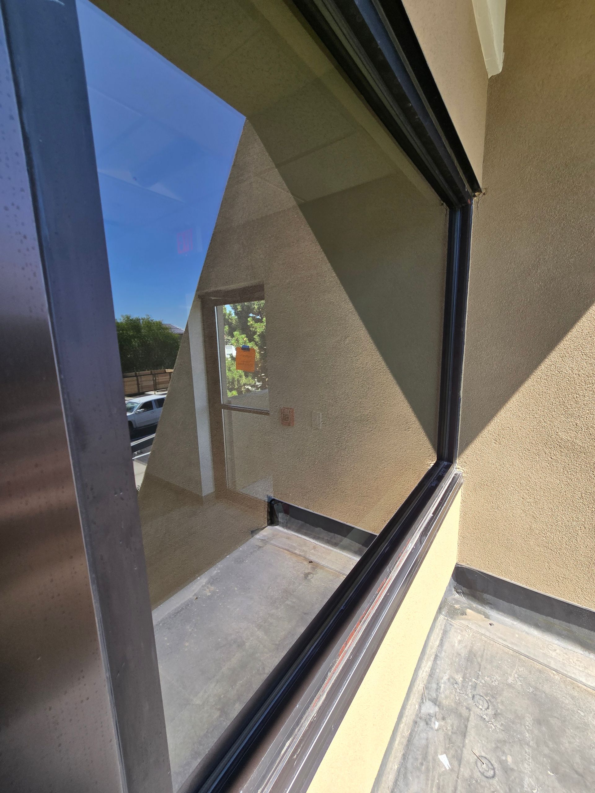 An angled view of a reflective storefront window showing a street scene, tan textured wall, and a side door.
