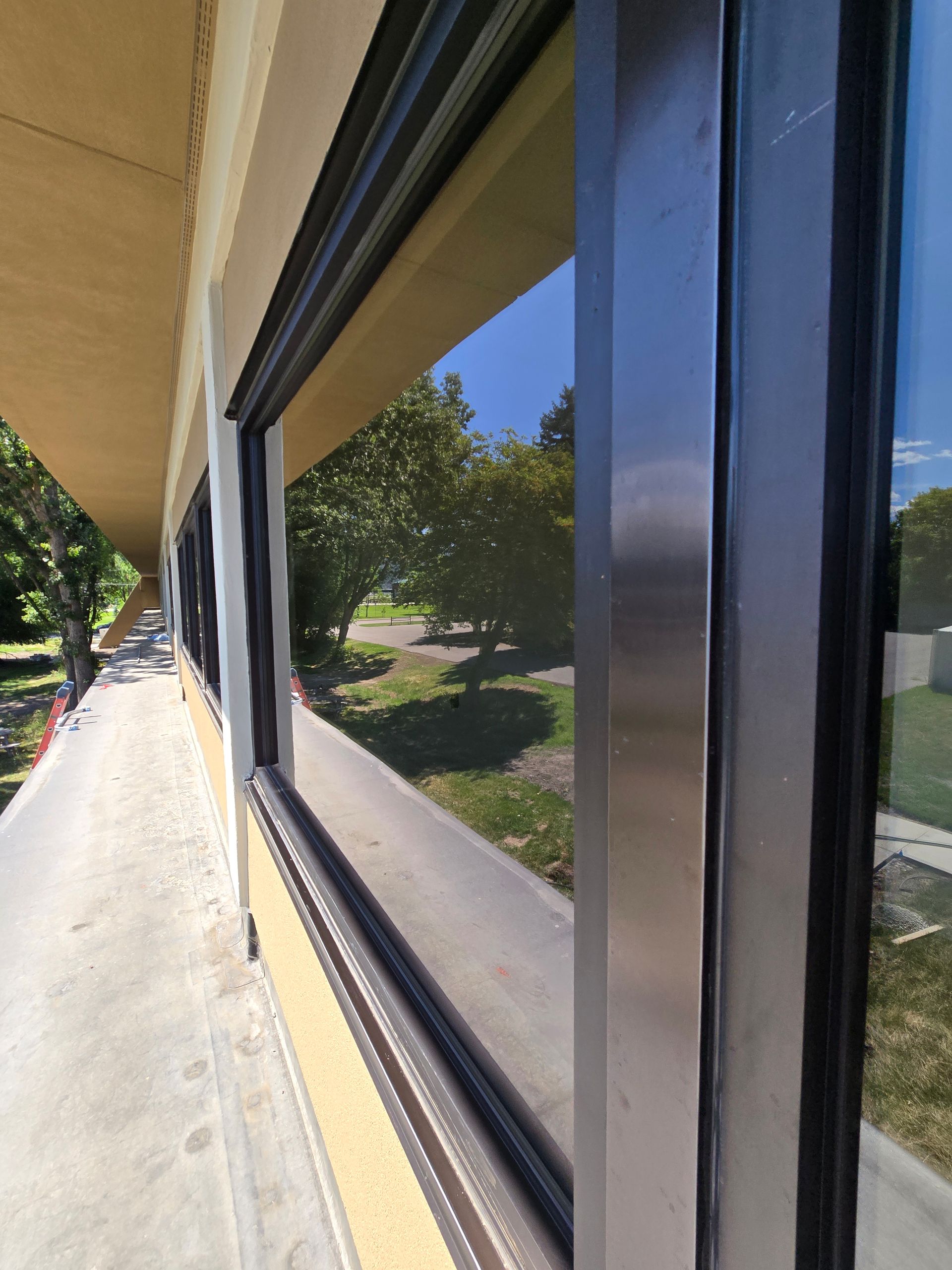 A low-angle view looking down a concrete walkway lined with large, reflective office windows under a beige overhang.