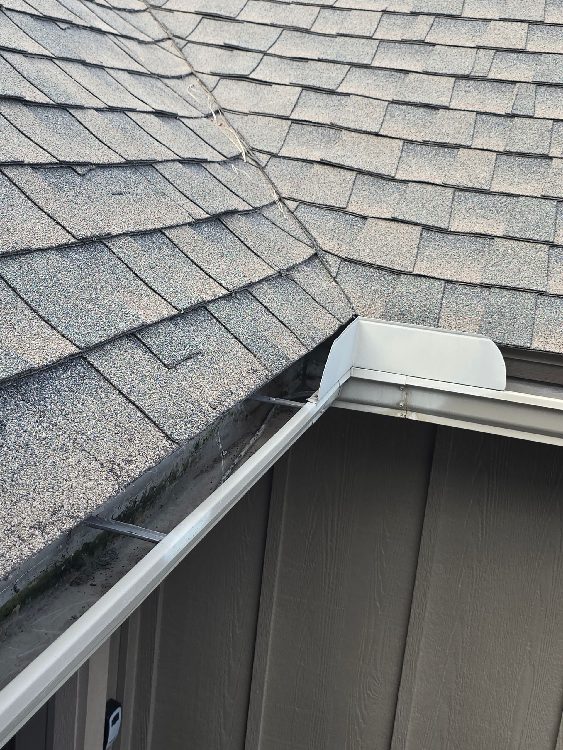 A white gutter splash guard installed at the corner of a residential roof where two shingled roof sections meet.
