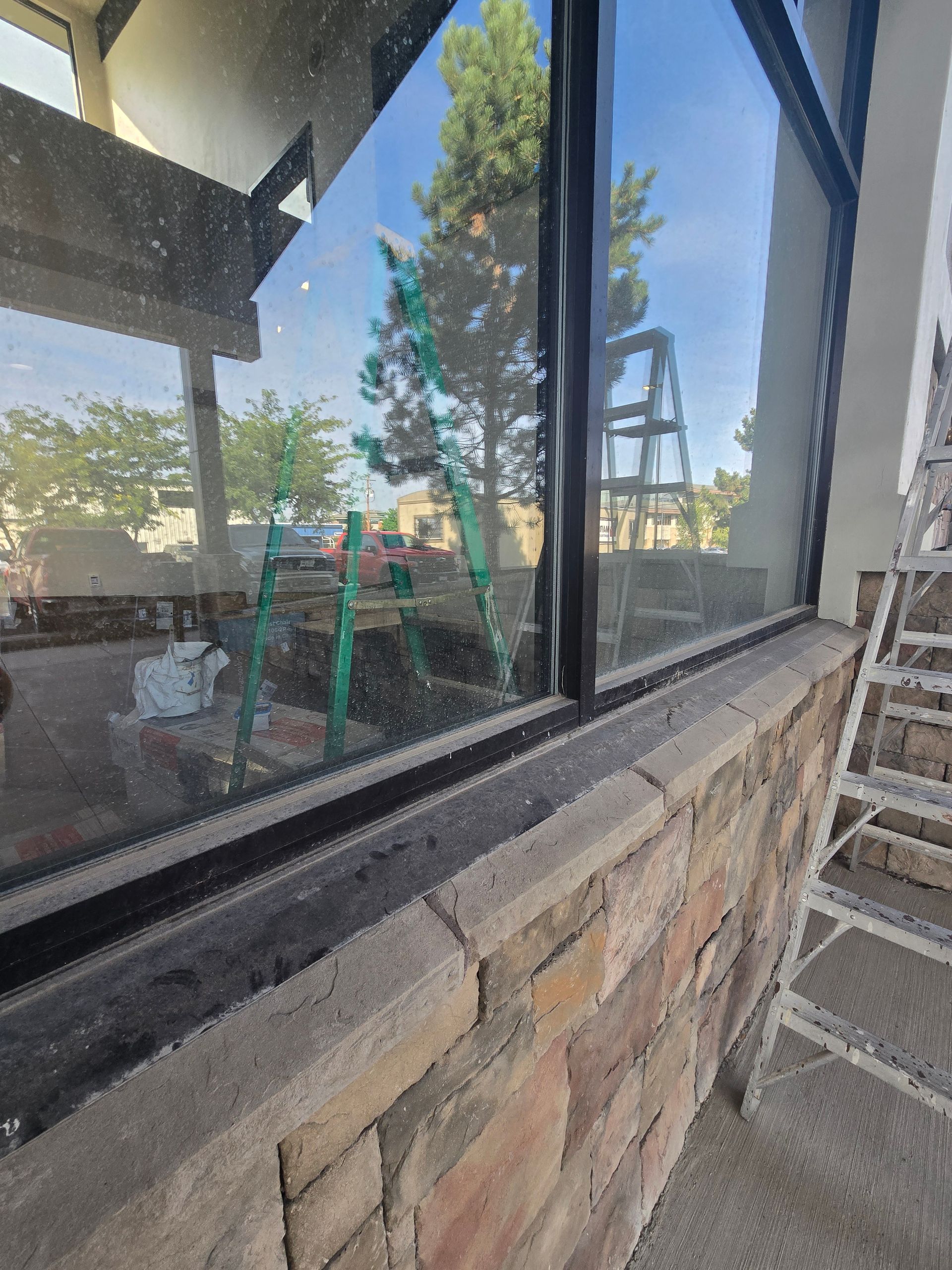 A low-angle view of a brick exterior wall topped with a large window, with a metal ladder visible to the right.