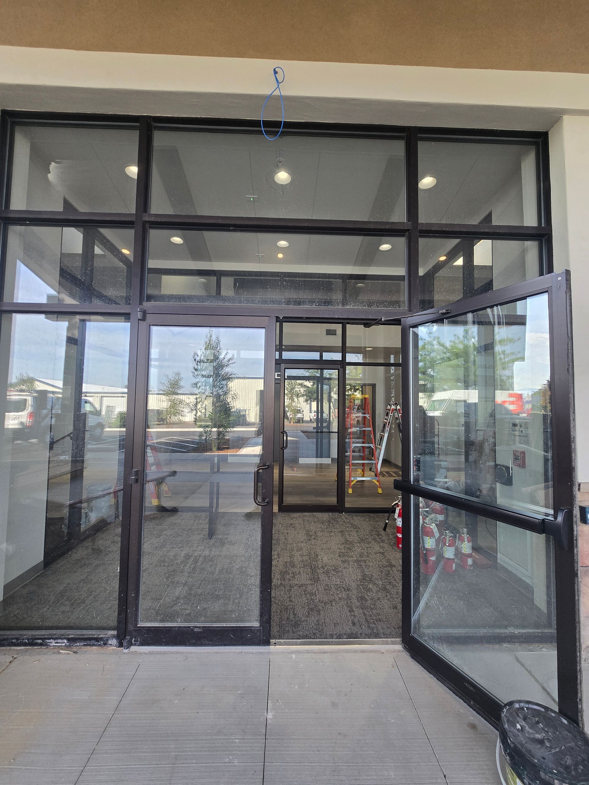 A set of glass double doors with black frames open into an interior space with recessed lighting and a carpeted floor.