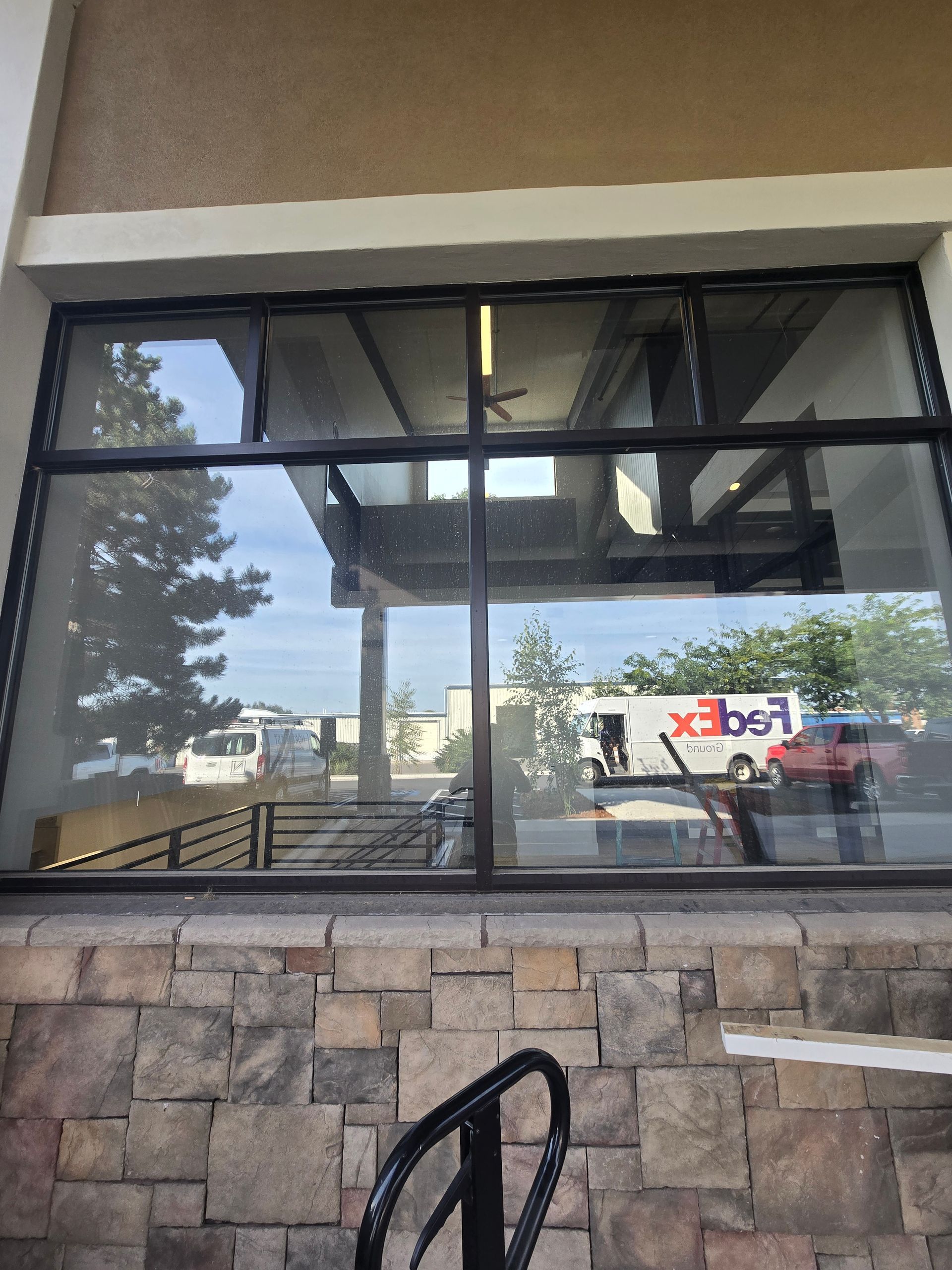 A view through a storefront window showing a reflection of a parking lot with a parked FedEx truck and a red vehicle.