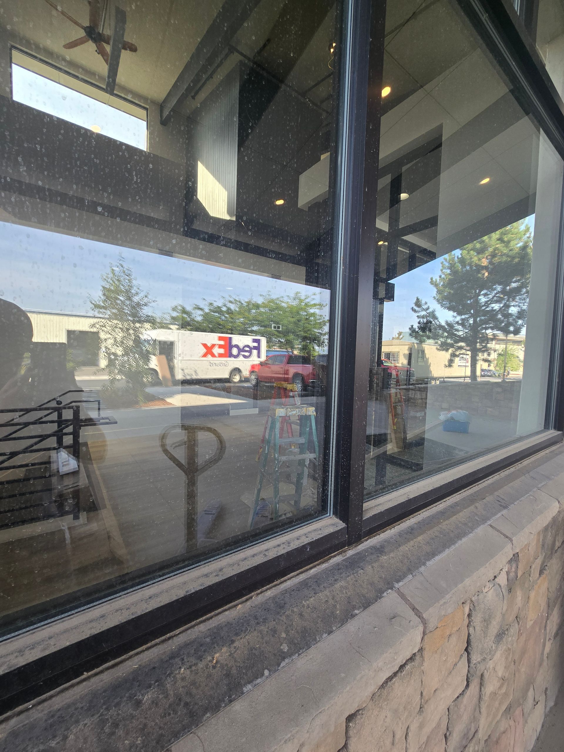 View through a large glass window showing a parked FedEx truck and a red car outside against a landscape with trees.