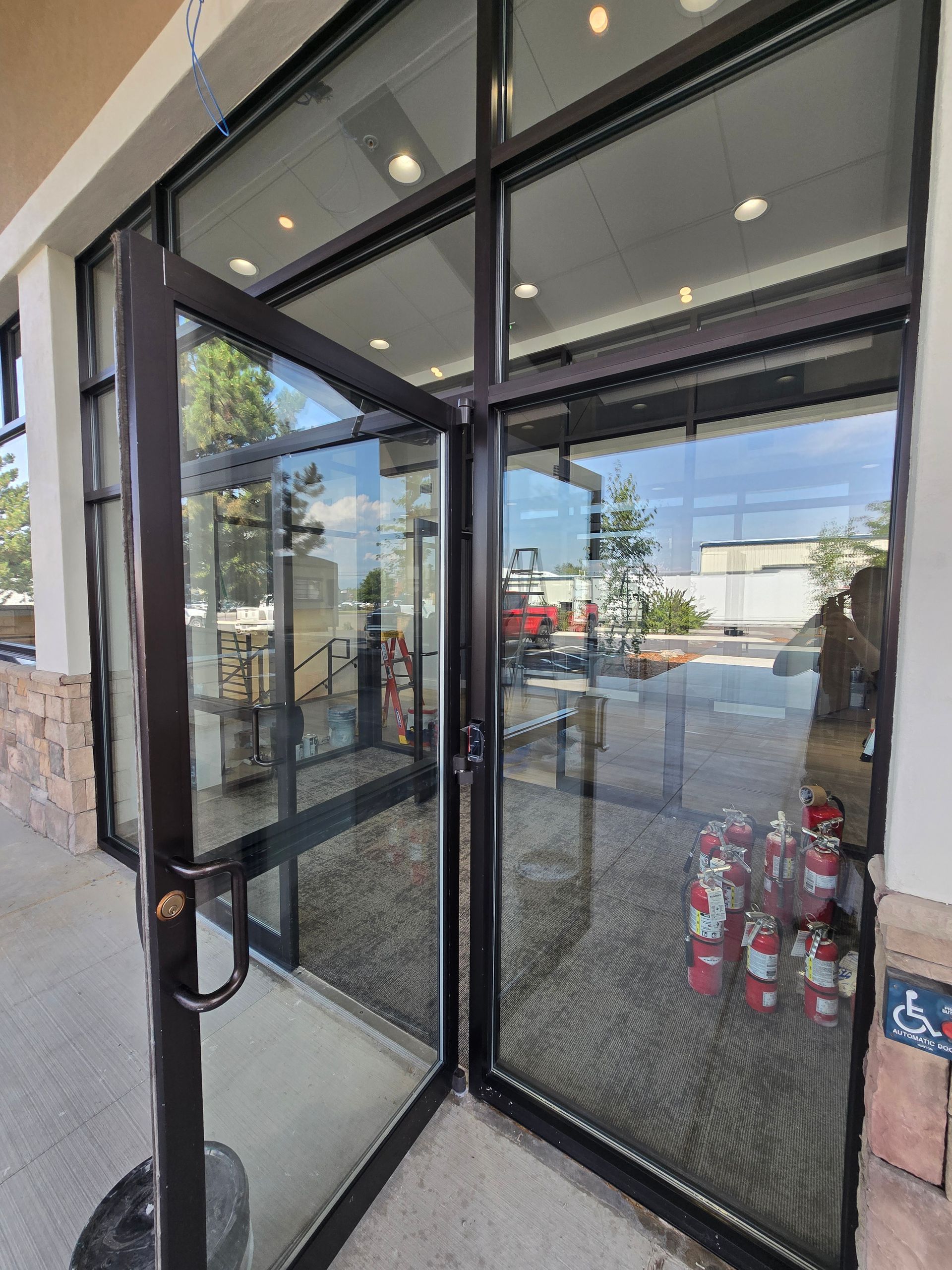 A pair of glass double doors with black metal frames at a building entrance, with a pile of fire extinguishers inside.