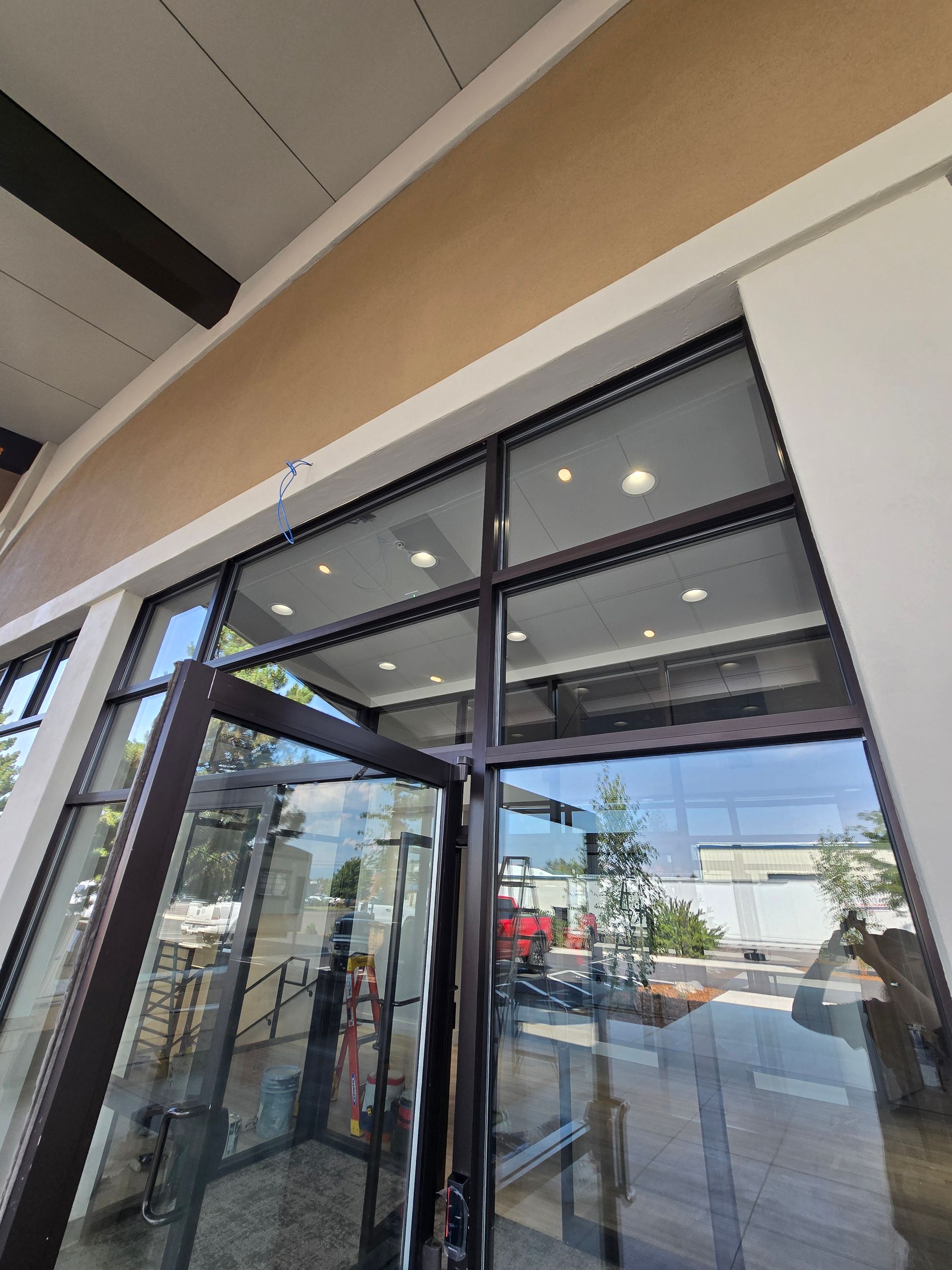 A wide-angle, low-angle view of a modern glass entrance door and storefront window set against a tan exterior wall.