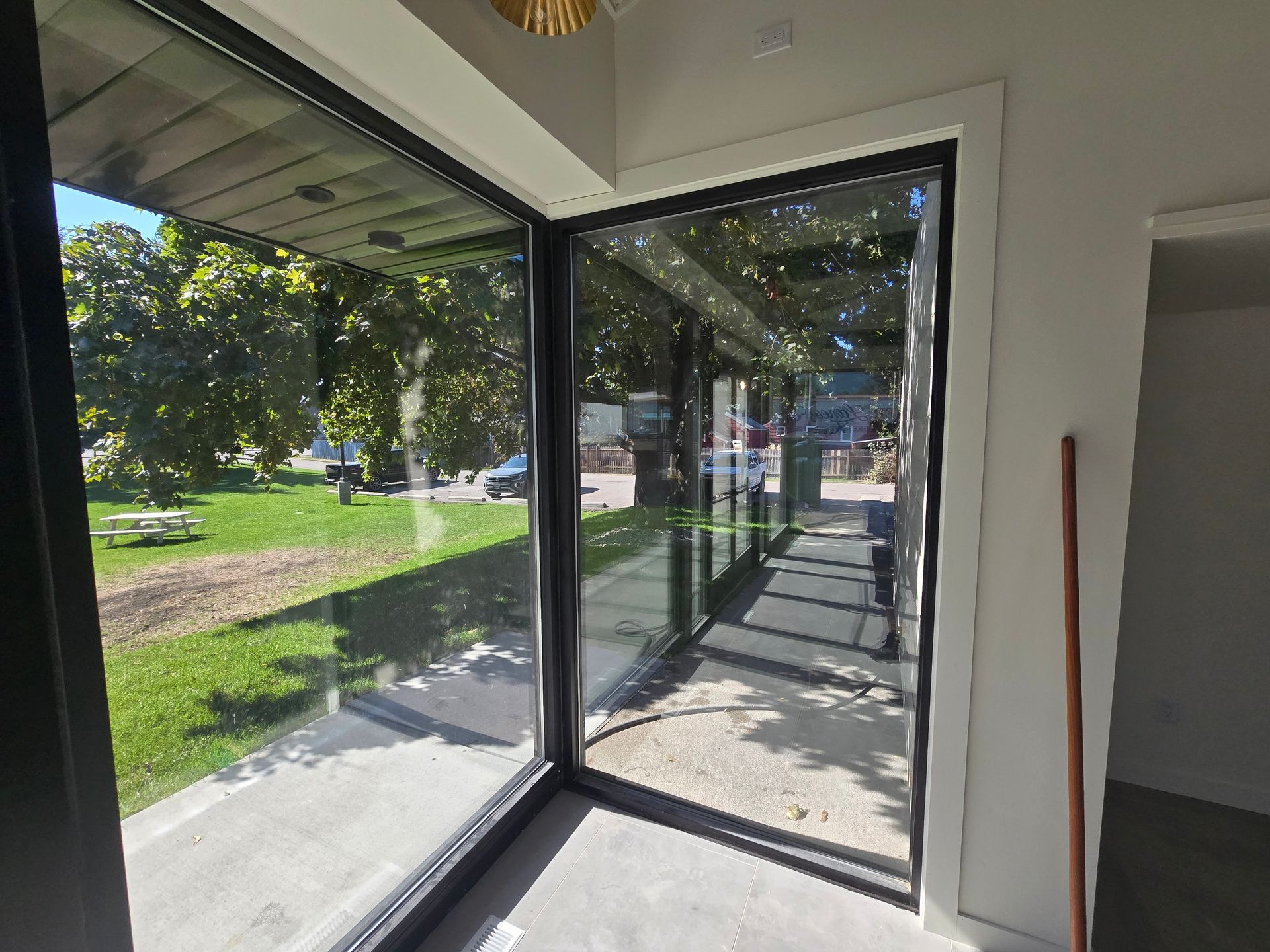 A bright corner with large, floor-to-ceiling windows showing an outdoor grassy area, paved walkway, and trees.
