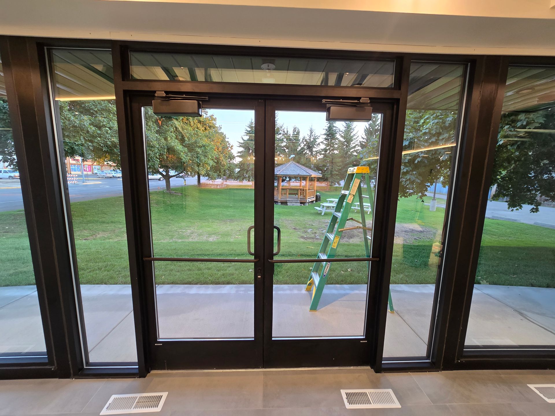 Double glass doors open to a view of a green lawn, trees, a gazebo, and a green ladder leaning against a window.