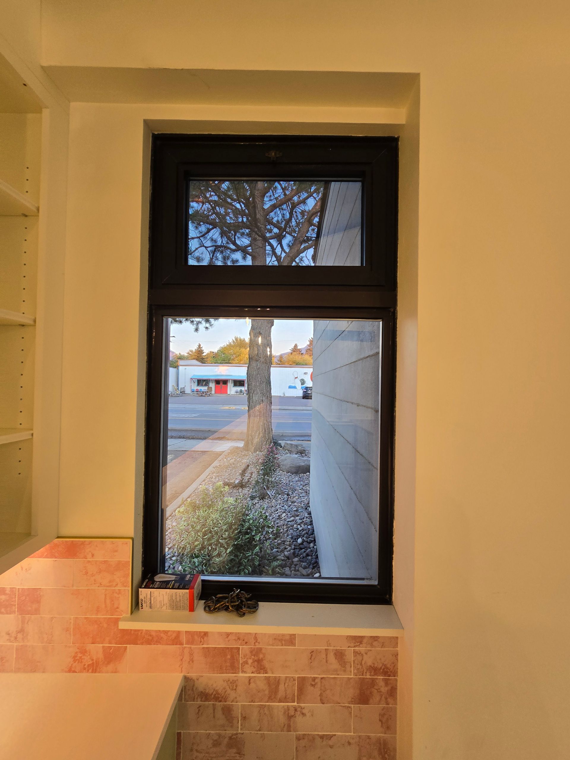 A dark-framed, double-hung window set into a light-colored wall above a pink tiled backsplash.