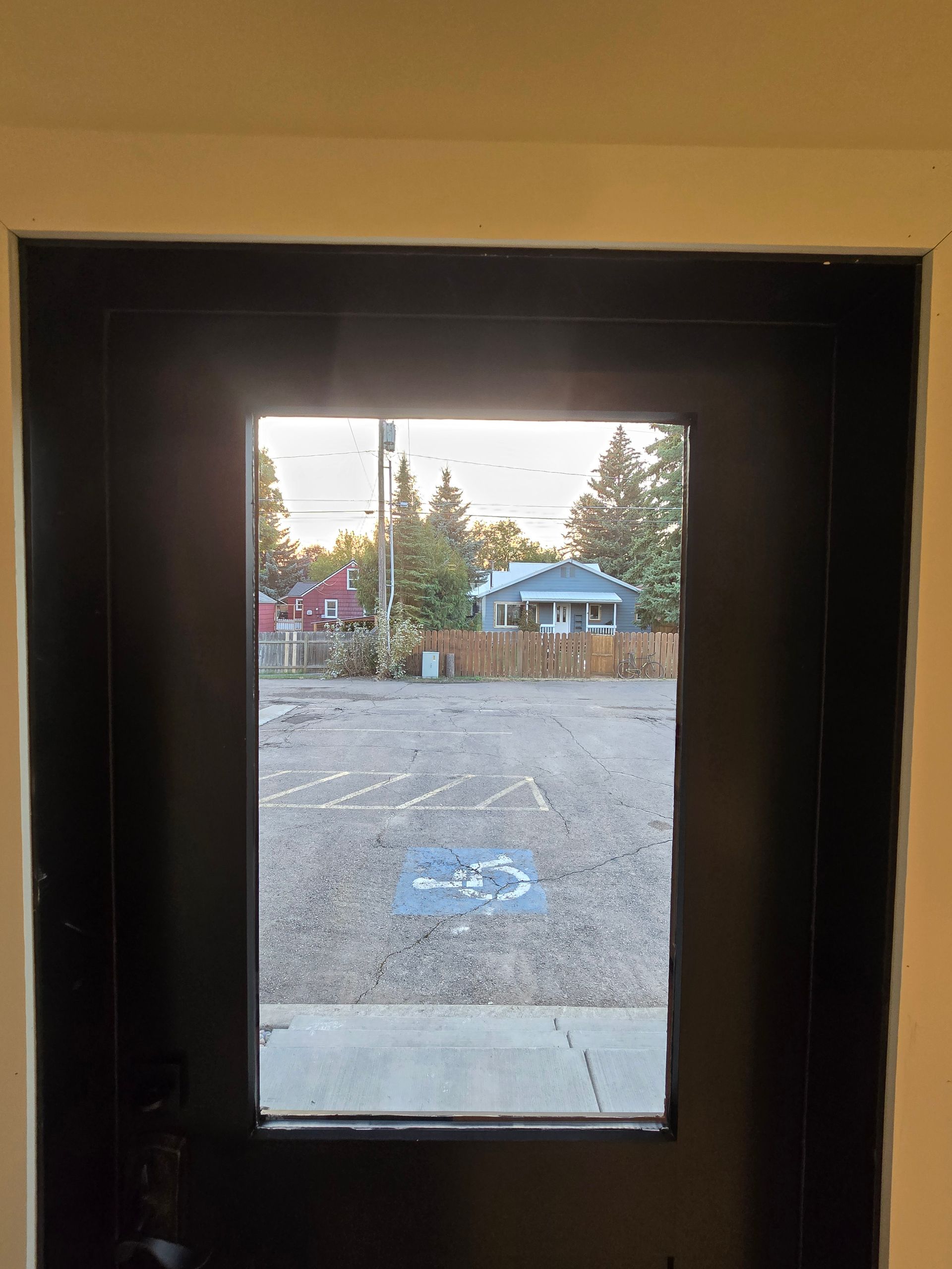 A view through a black door window showing a gravel lot with a blue wheelchair accessible symbol and a house in the back.