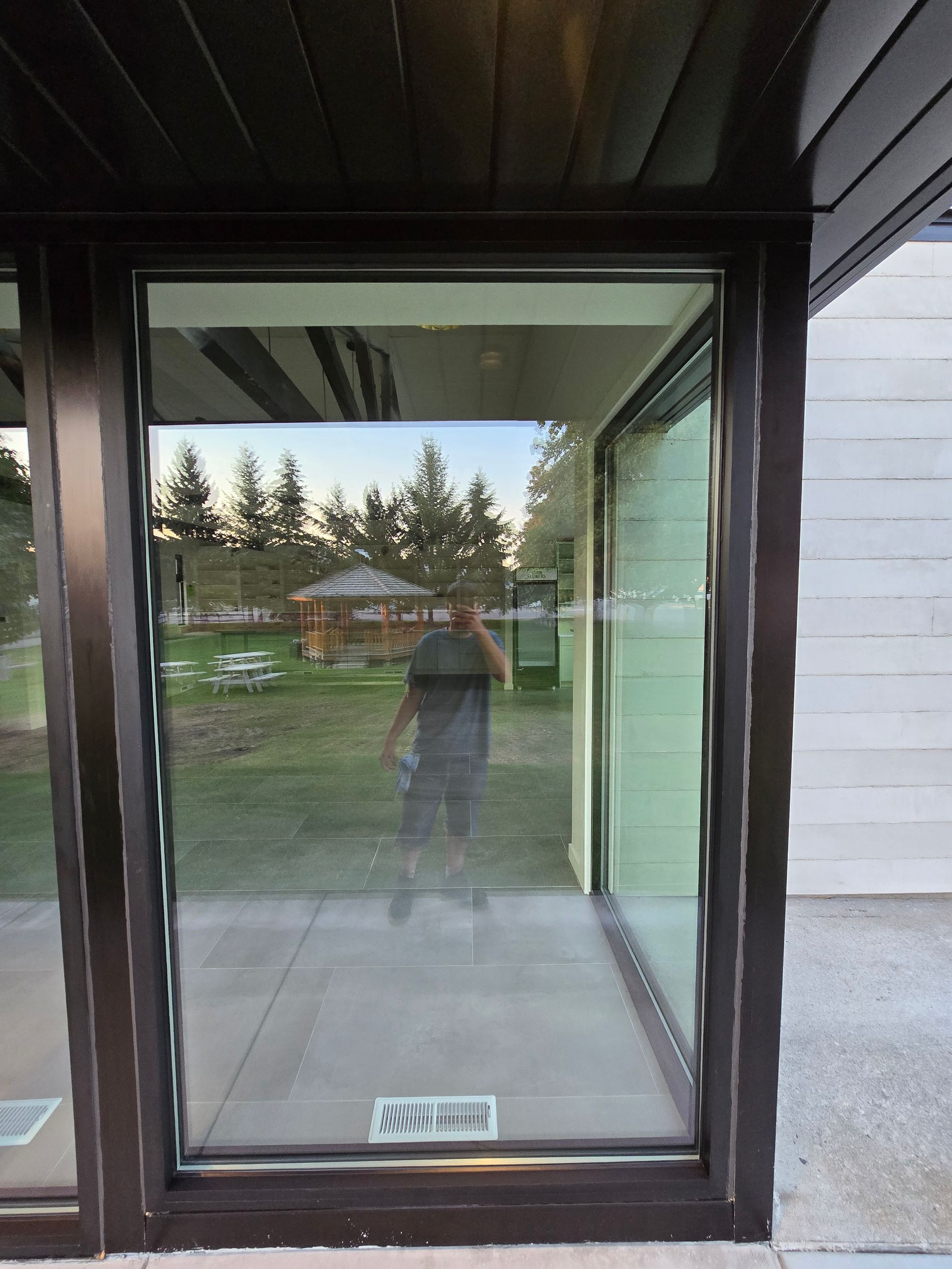 A person stands behind a large glass door, reflecting a grassy backyard with trees and a small structure.
