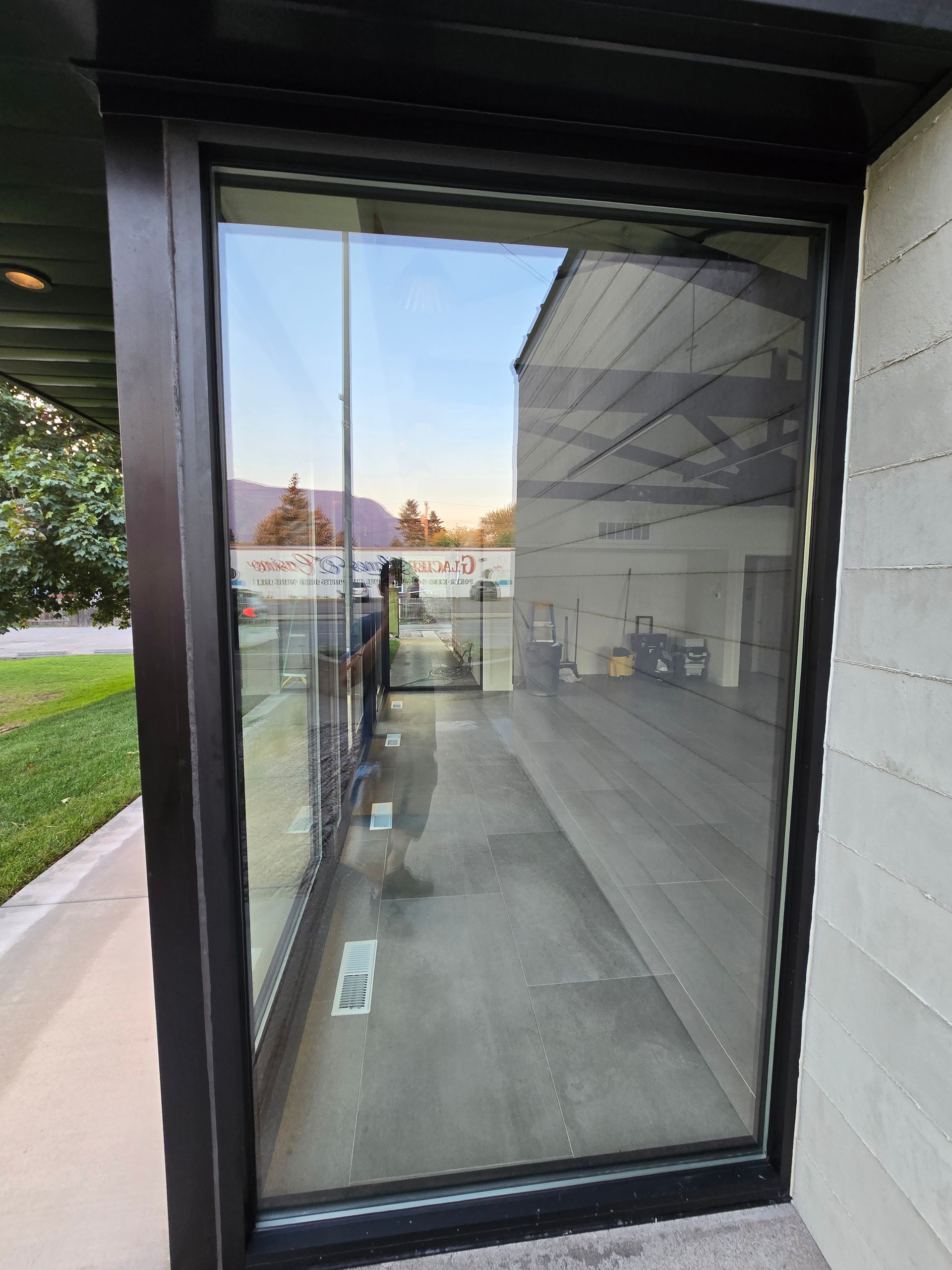 A view through a large glass storefront window into an empty, well-lit interior with a gray floor.