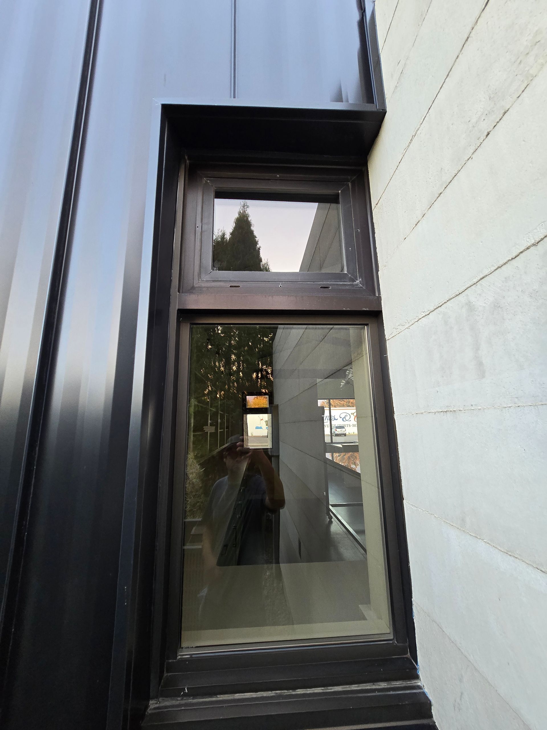 A dark-framed window recessed into a black metal wall next to a light-colored, textured concrete wall.