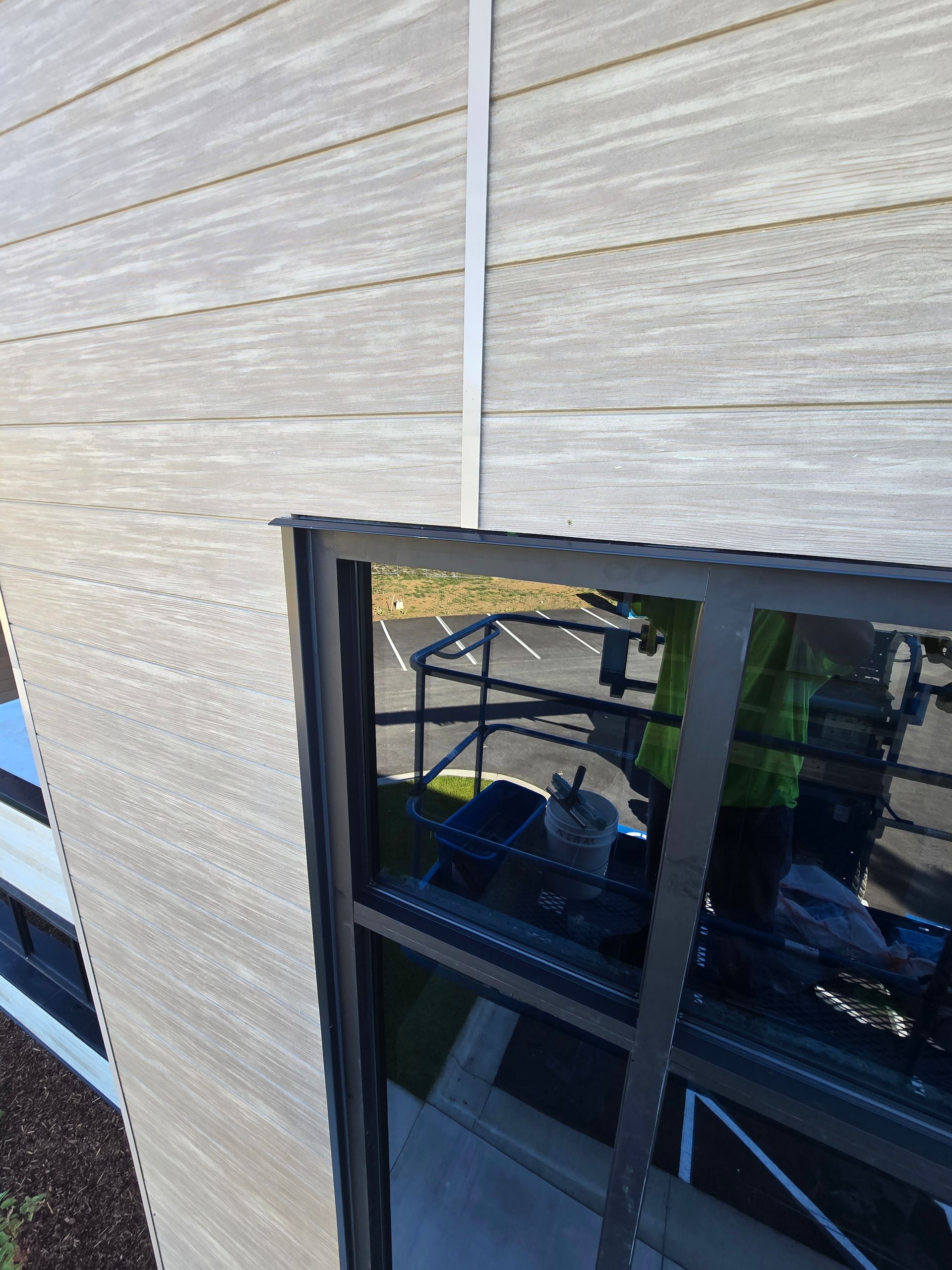 Exterior view of a dark window frame installed in a building with light, horizontal wood-grain siding.
