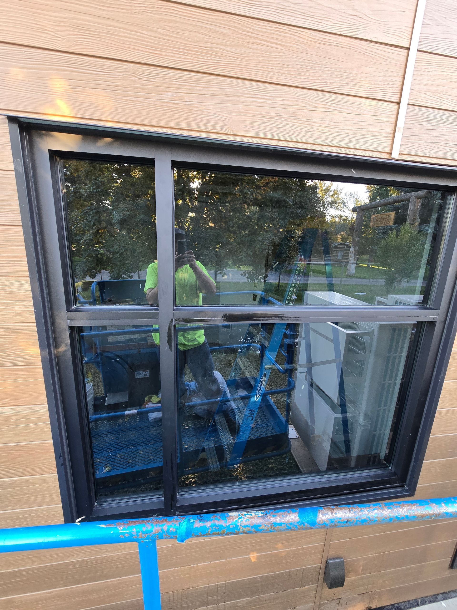 A worker in a high-visibility vest reflected in the window of a building with brown horizontal siding.