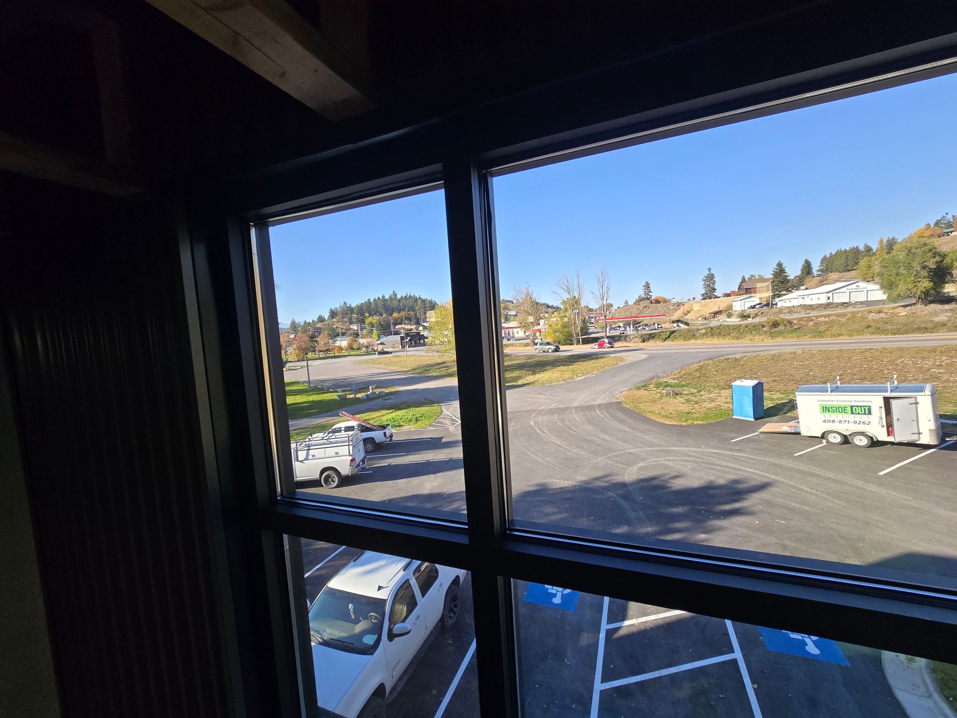 View from an interior window looking down at a parking lot with several parked vehicles and a small white trailer.