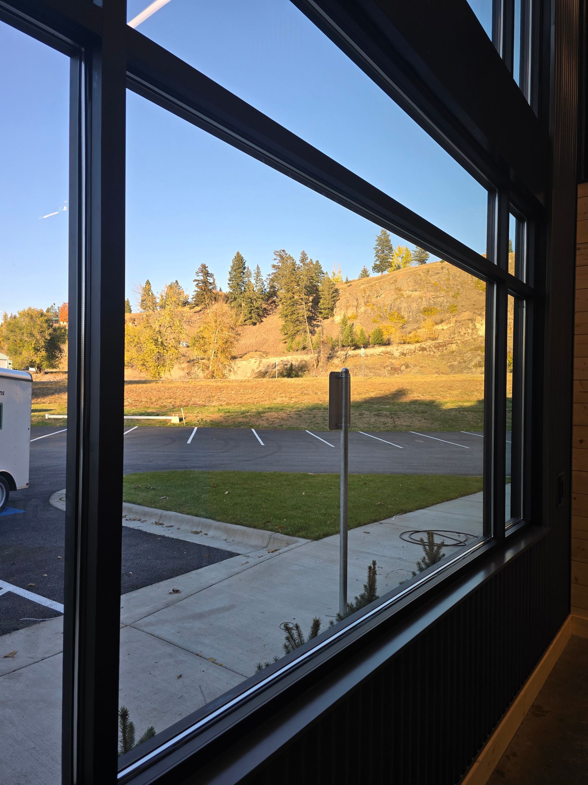 A view from inside through a window showing a sunny parking lot and a hillside with trees in autumn colors.