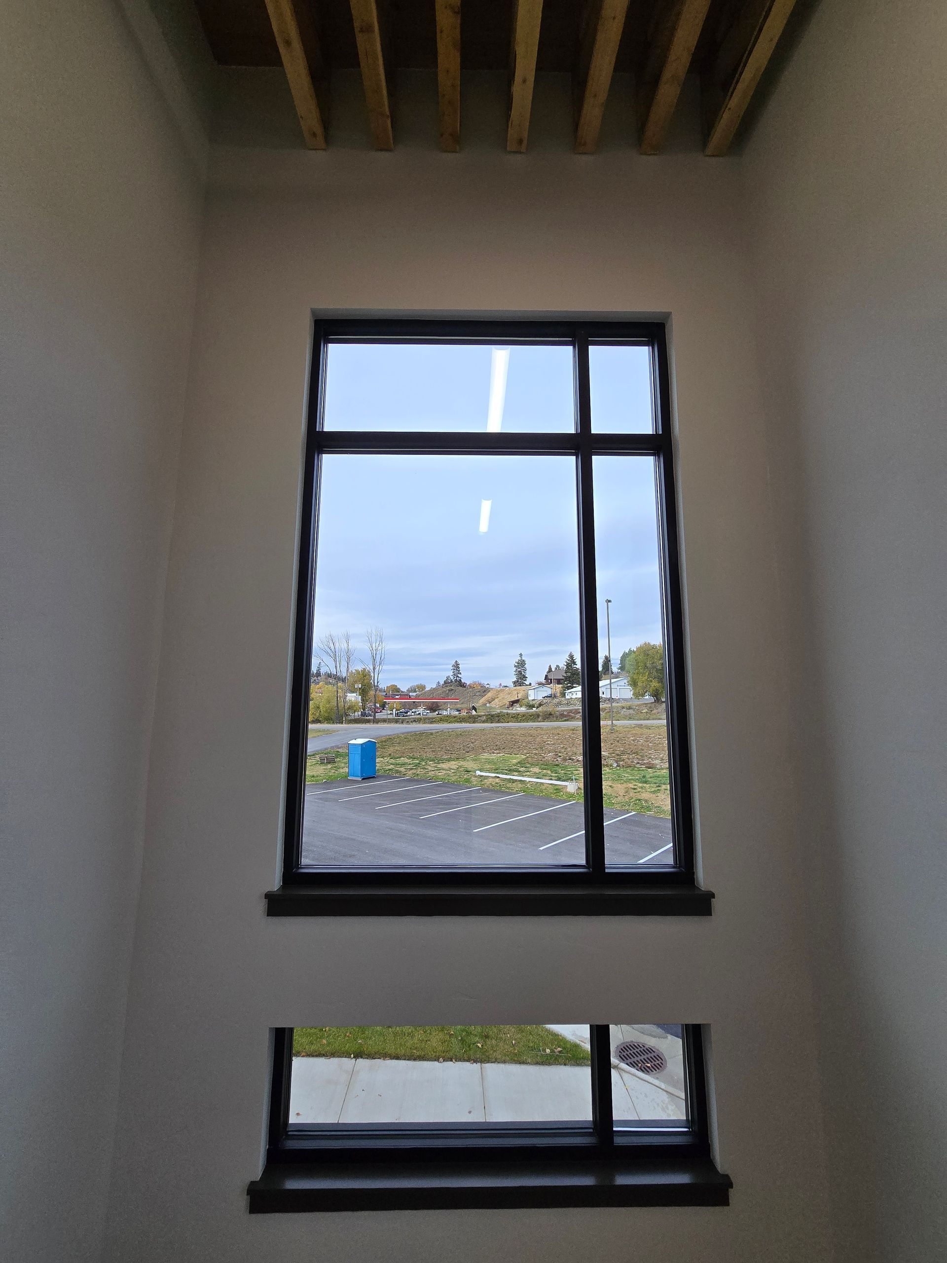 View through two stacked rectangular windows looking out onto a parking lot, grass, and trees under a cloudy sky.