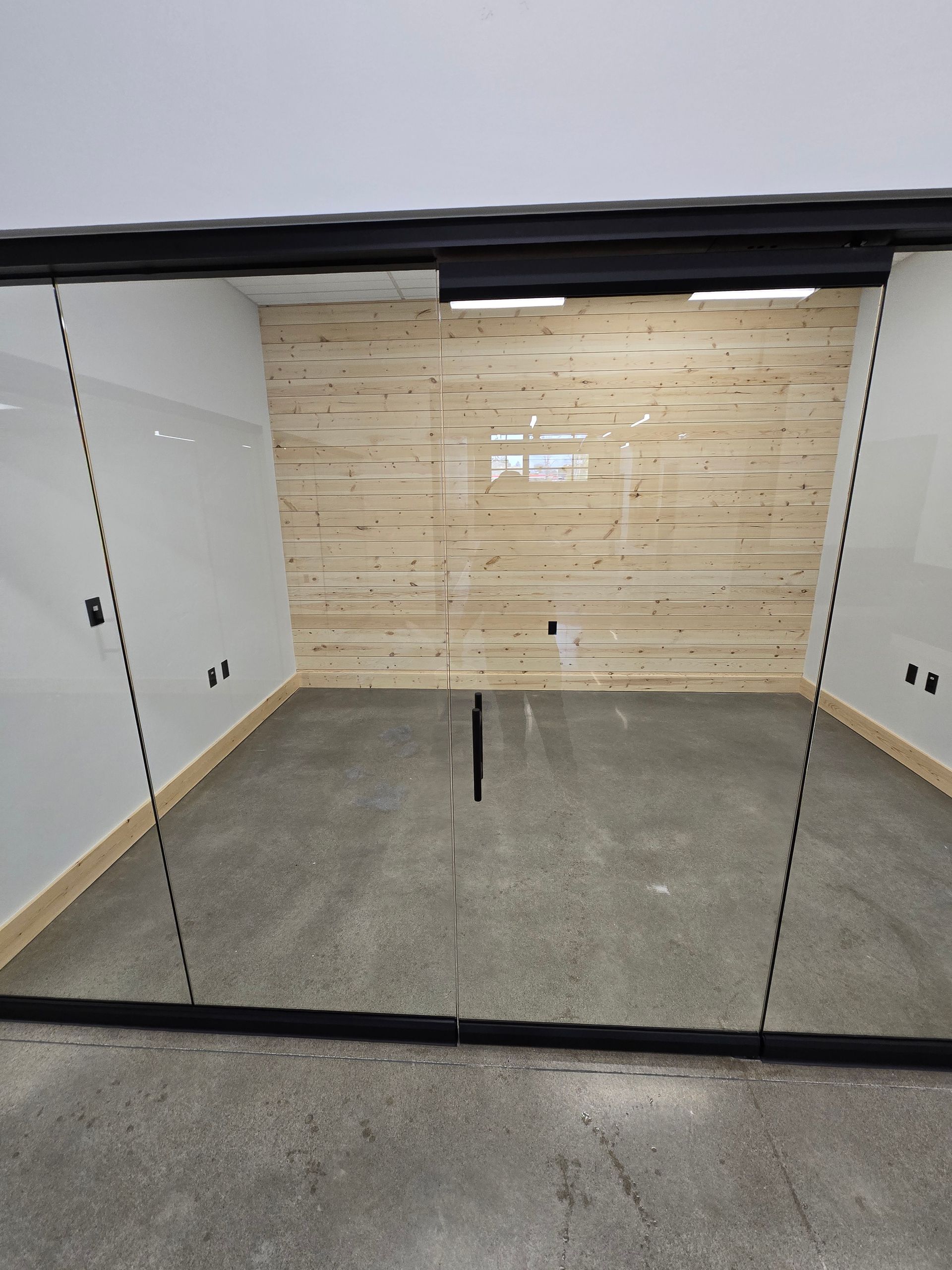 A glass-walled office with a light wood-plank back wall and concrete flooring, seen from the outside.