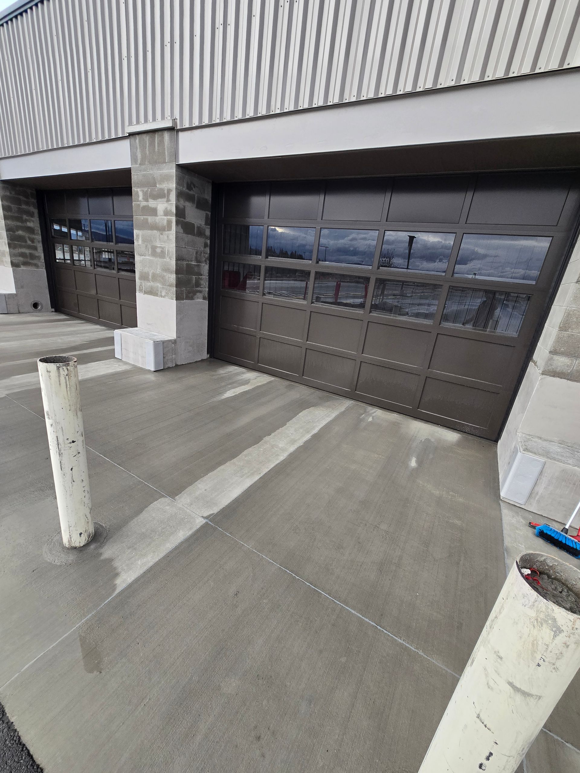 Two brown, glass-paneled garage doors set into a building exterior with light gray concrete and stone accents.